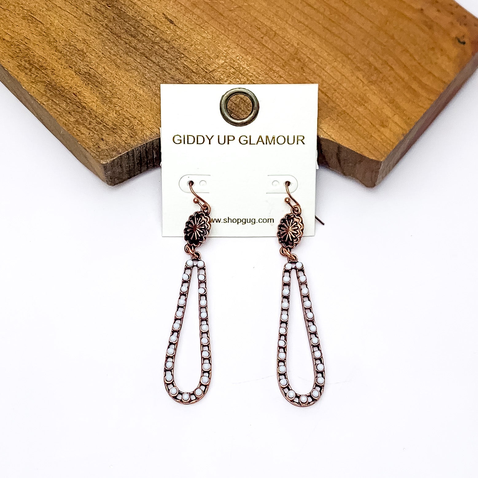 Copper Tone Open Teardrop Earrings With Small Stones in Ivory. Pictured on a white background with the earrings laying against a wood piece.