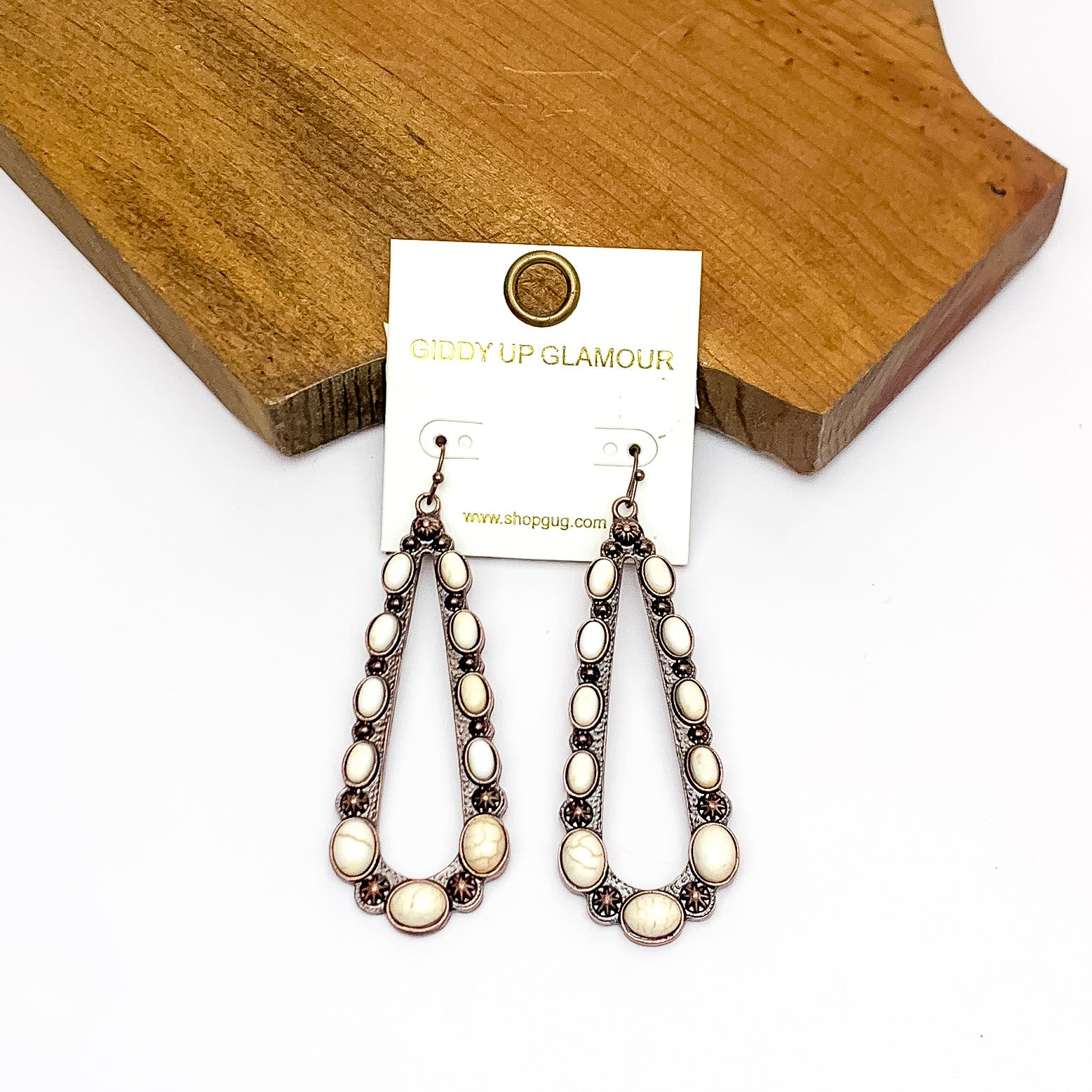 Copper Tone Open Teardrop Earrings With Stones in Ivory. Pictured on a white background with the earrings laying against a wood piece.