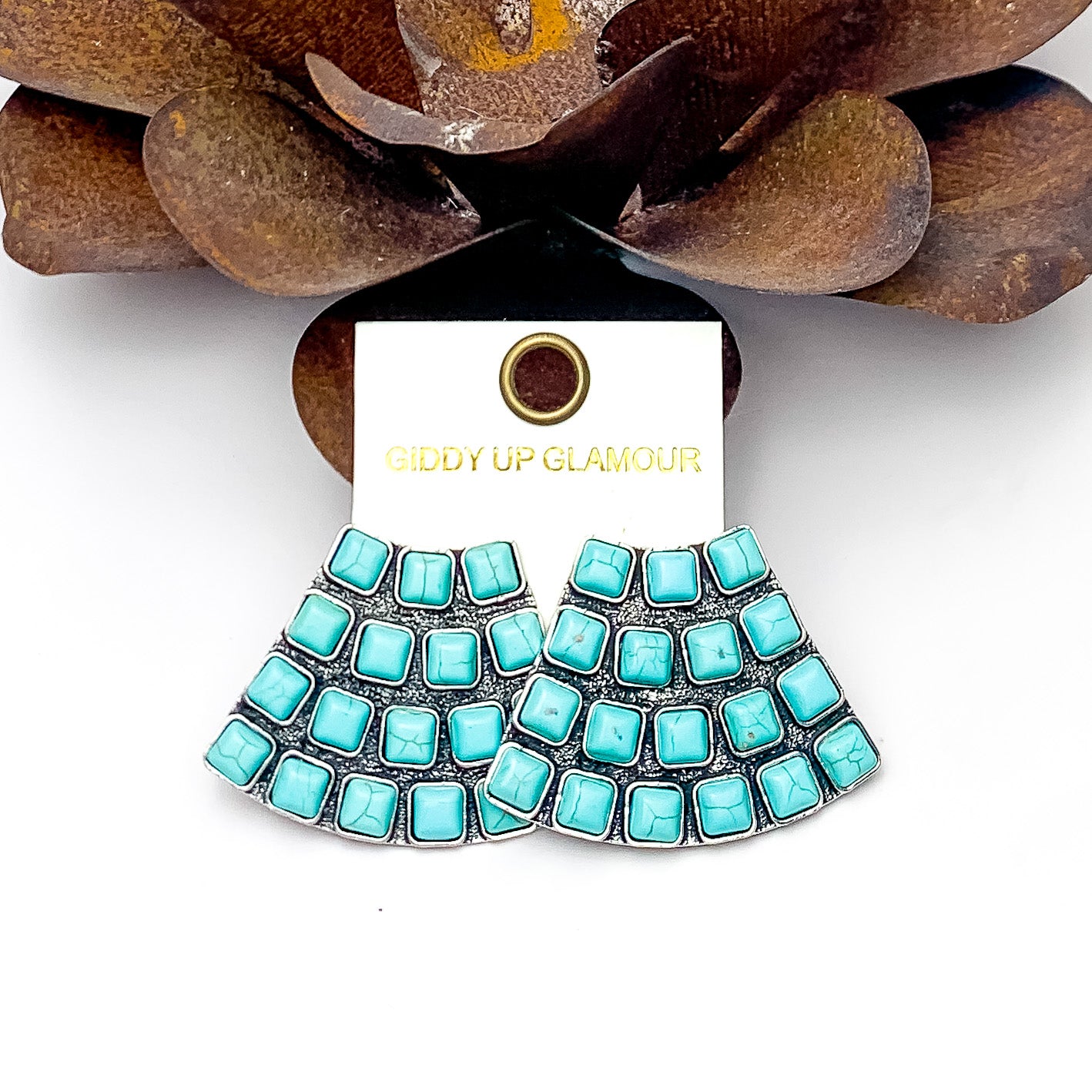 Western Trapezoid Shape Silver Tone With Stones in Turquoise. Pictured on a white background with a metal flower behind the earrings.