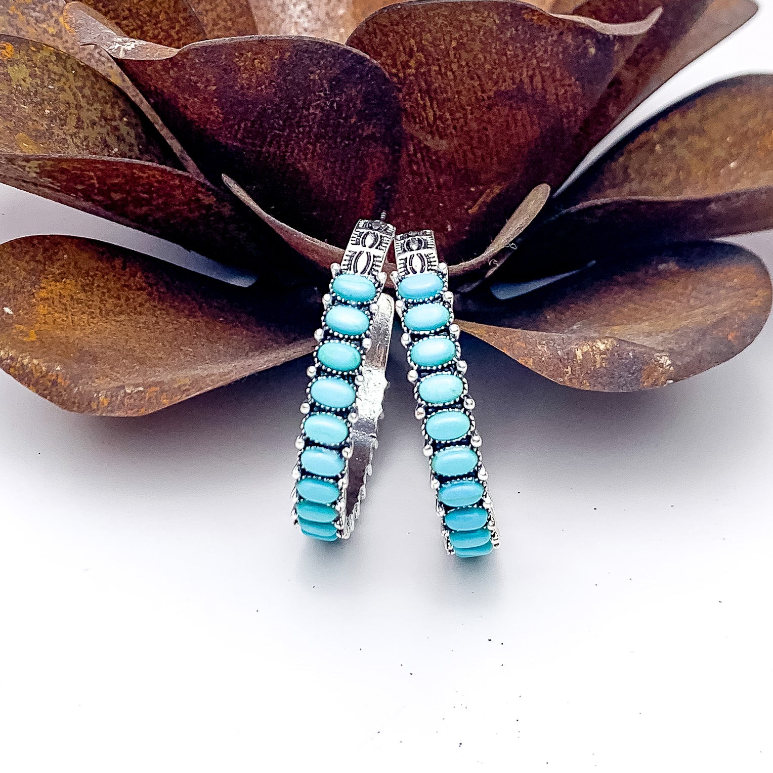 Silver Tone Semi Hoop Earring with Turquoise Stones. Pictured on a white background with the earrings against a metal flower.