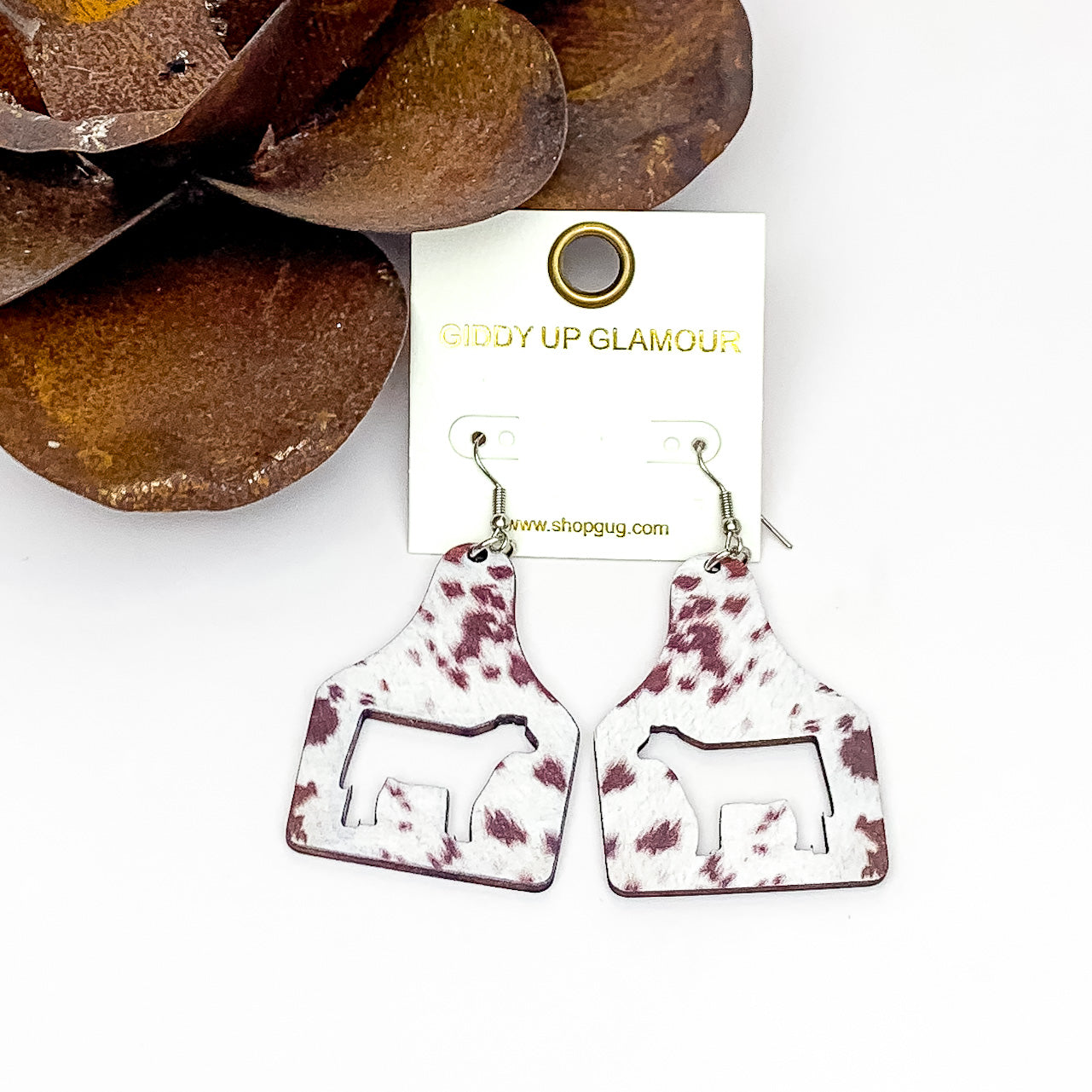Cattle Tag Wooden Earrings in Cow Print. Pictured on a white background with the rose in the top left corner.