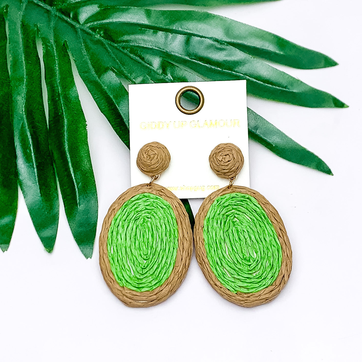 Brunch Bash Raffia Wrapped Oval Earrings in Light Green. Pictured on a white background with the earrings on a leaf.