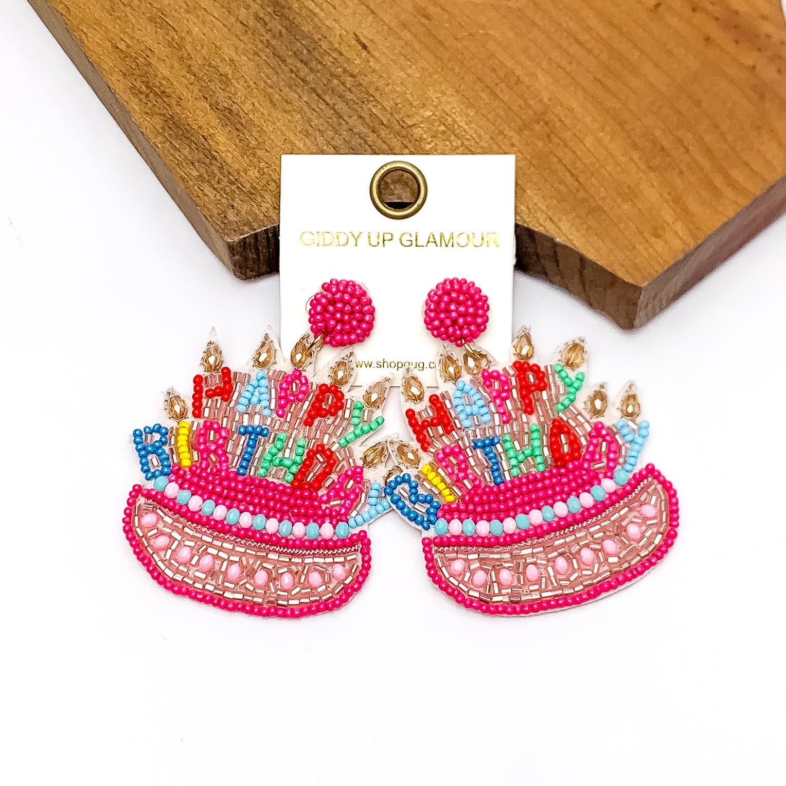 Happy Birthday Cake Beaded Earrings in Pink. Pictured on a white background with the earrings laying on a piece of wood.