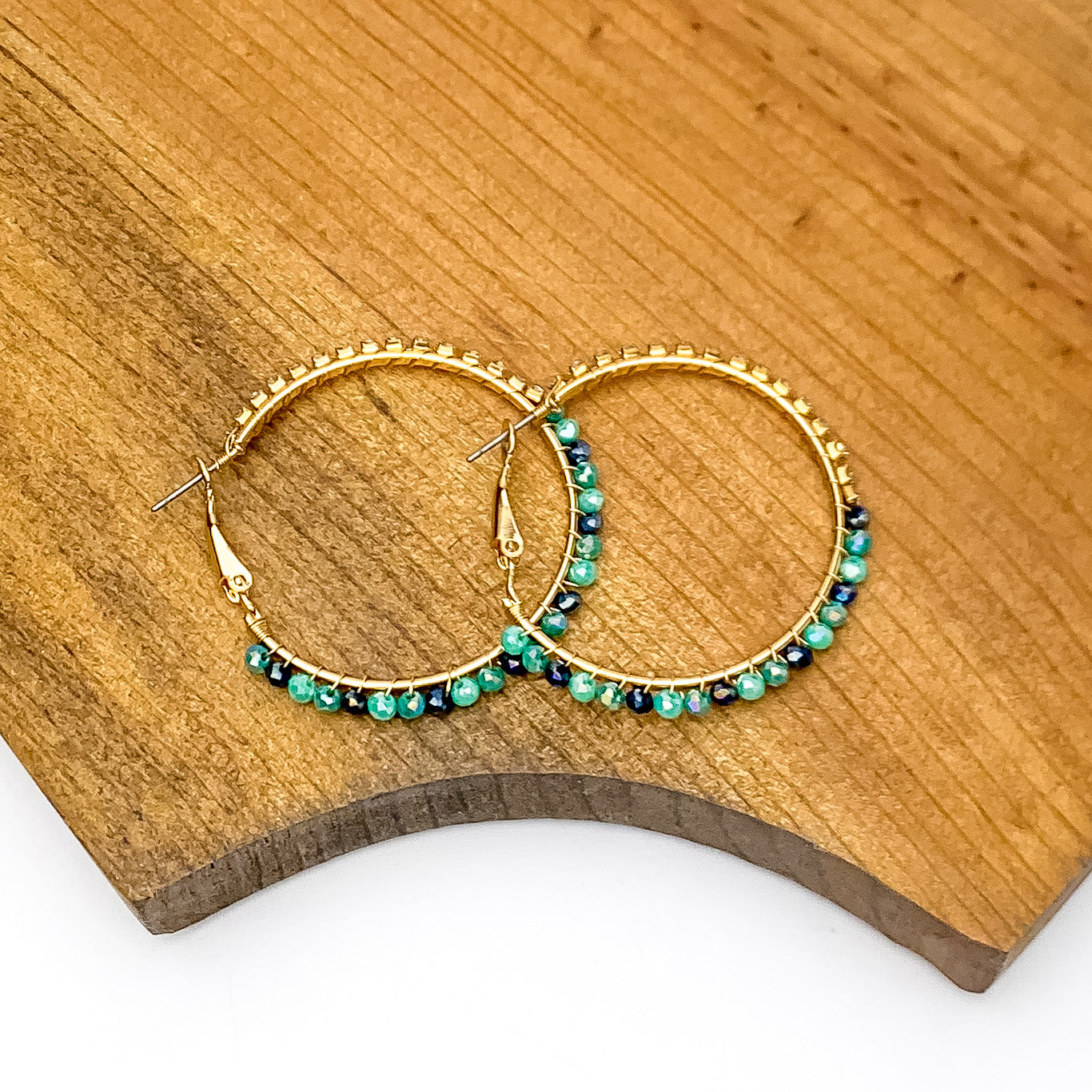 Gold Tone Hoop Earrings Wrapped in Clear and Blue Crystals. Pictured on a piece of wood.