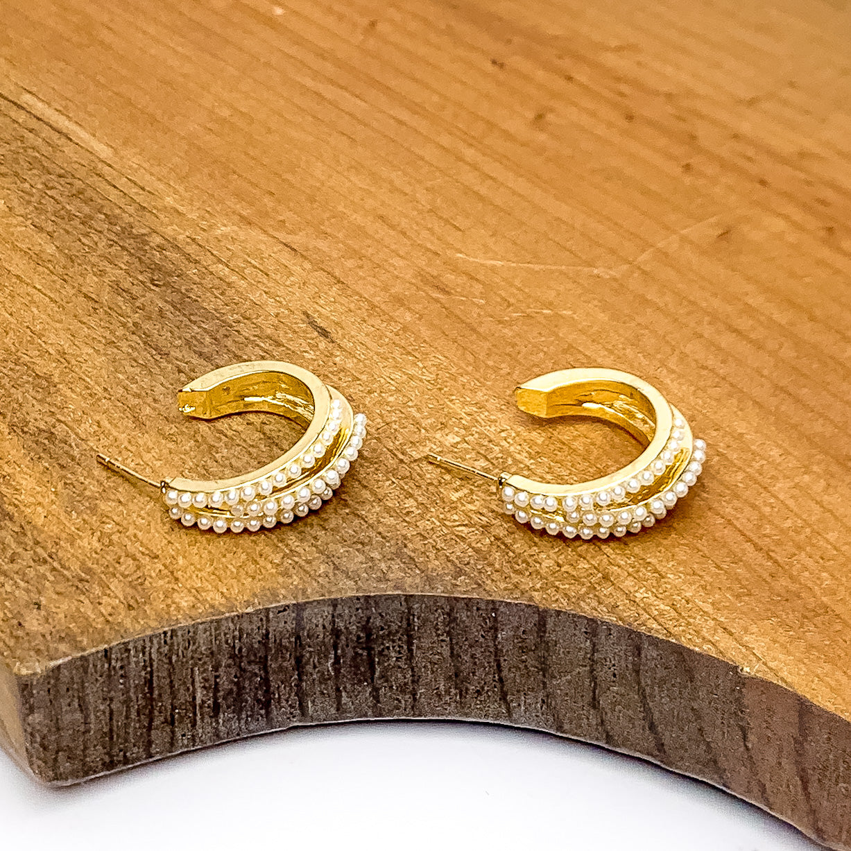 Small Gold Tone Hoop Earrings Outlined in Pearls. Pictured on a piece of wood.
