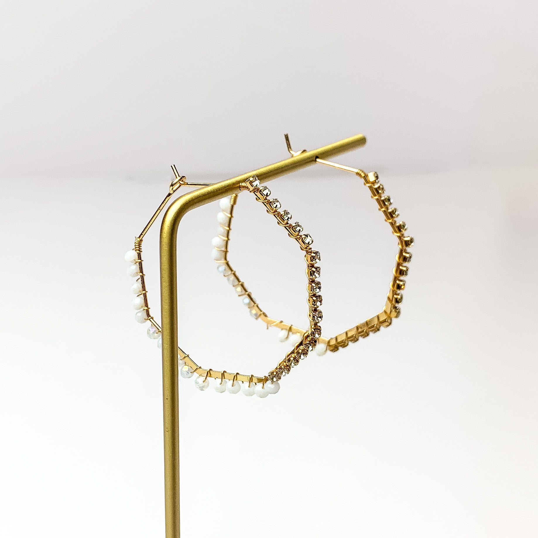 Small Gold Tone Hoop Earrings Outlined in Pearls. Pictured on a white background with the earrings on a gold stand.
