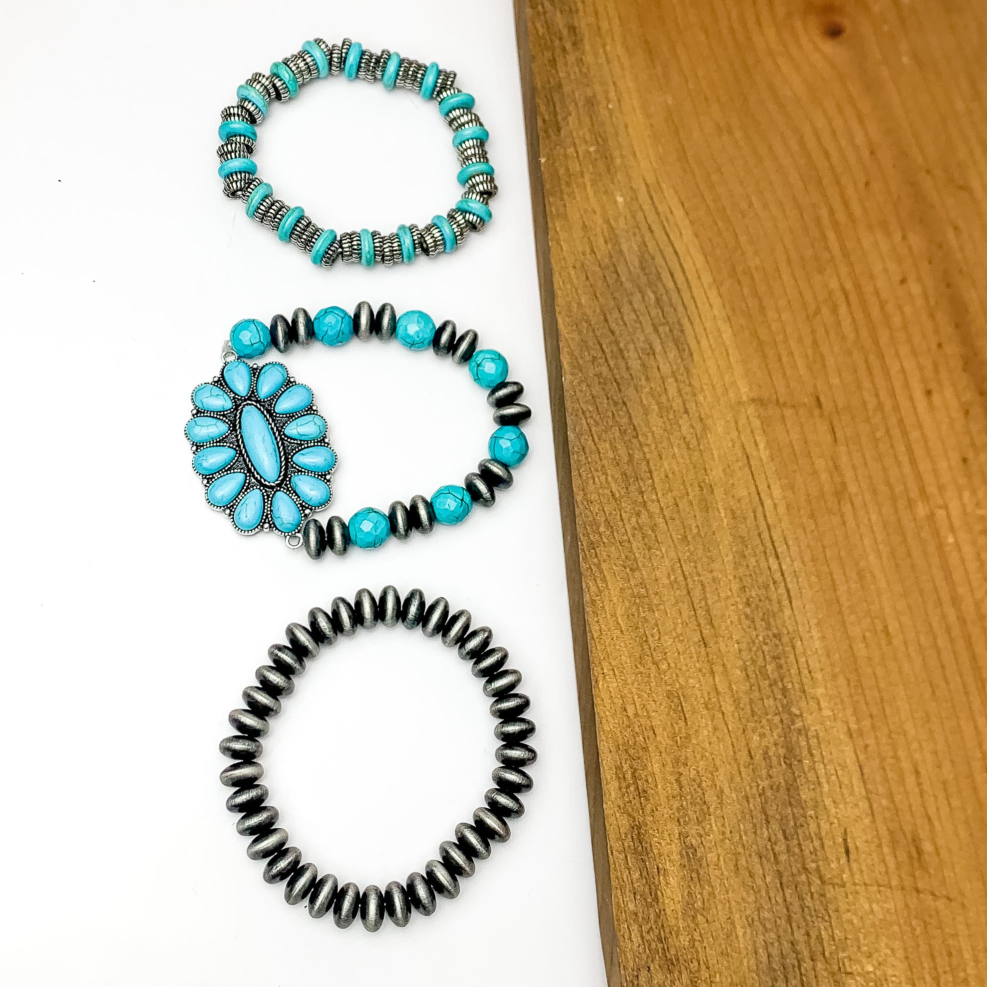 Set of Three | Silver Tone Bracelets With Turquoise Stones. Pictured on a white background with wood on the right side.