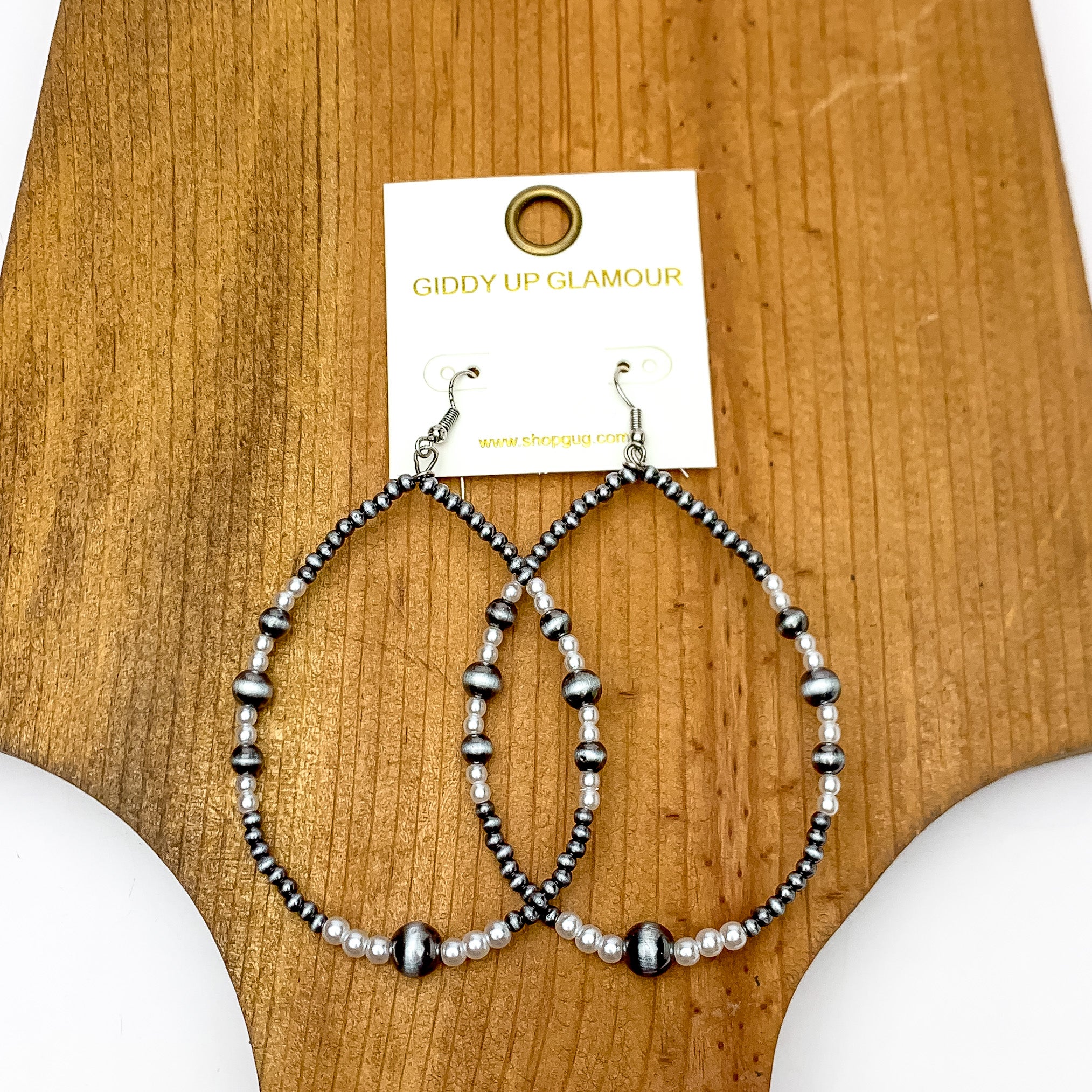 Open Teardrop Earrings With Beads in Silver Tone and White. Pictured on a white background with the earrings on a wood piece.