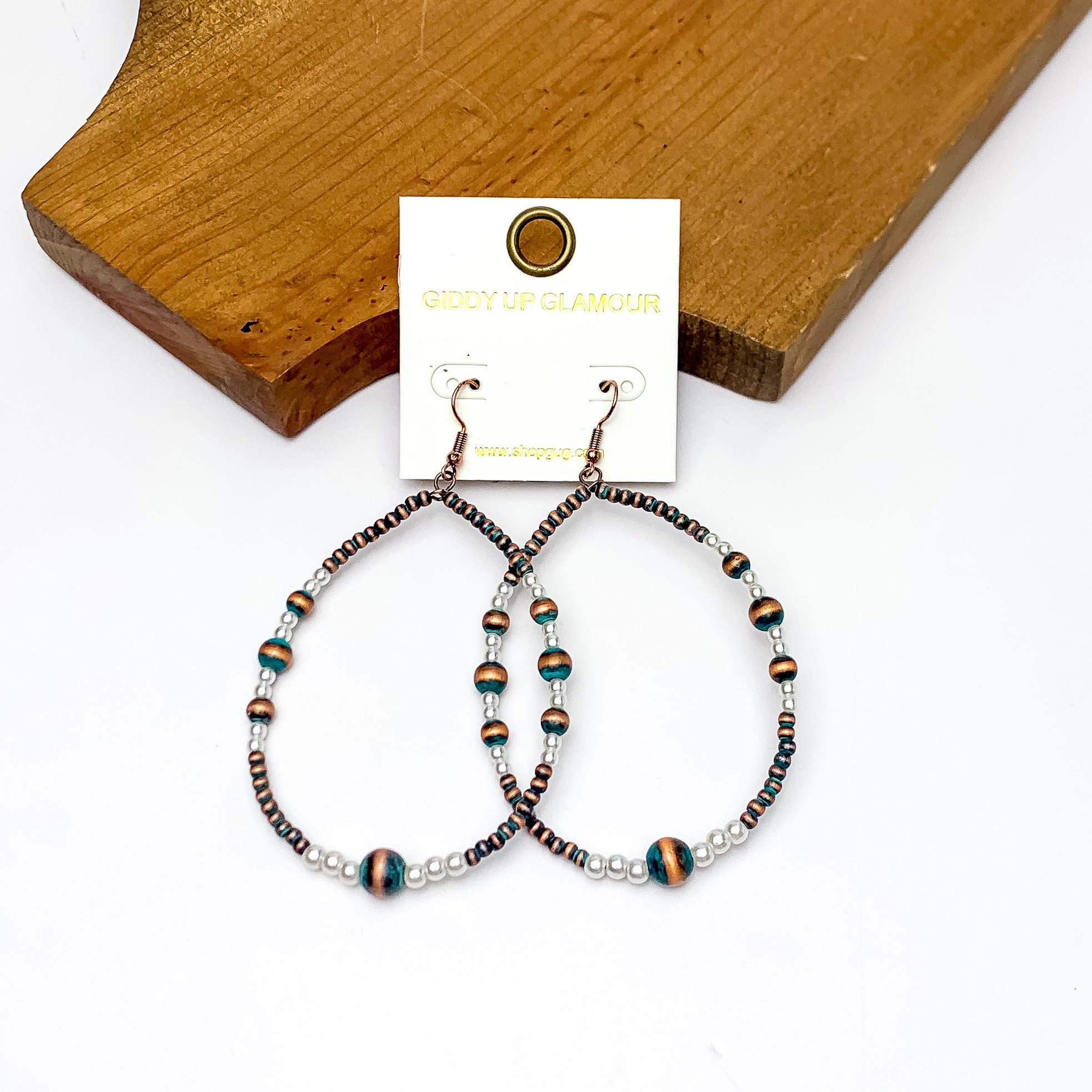 Open Teardrop Earrings With Beads in Patina and White. Pictured on a white background with the earrings against a wood piece.