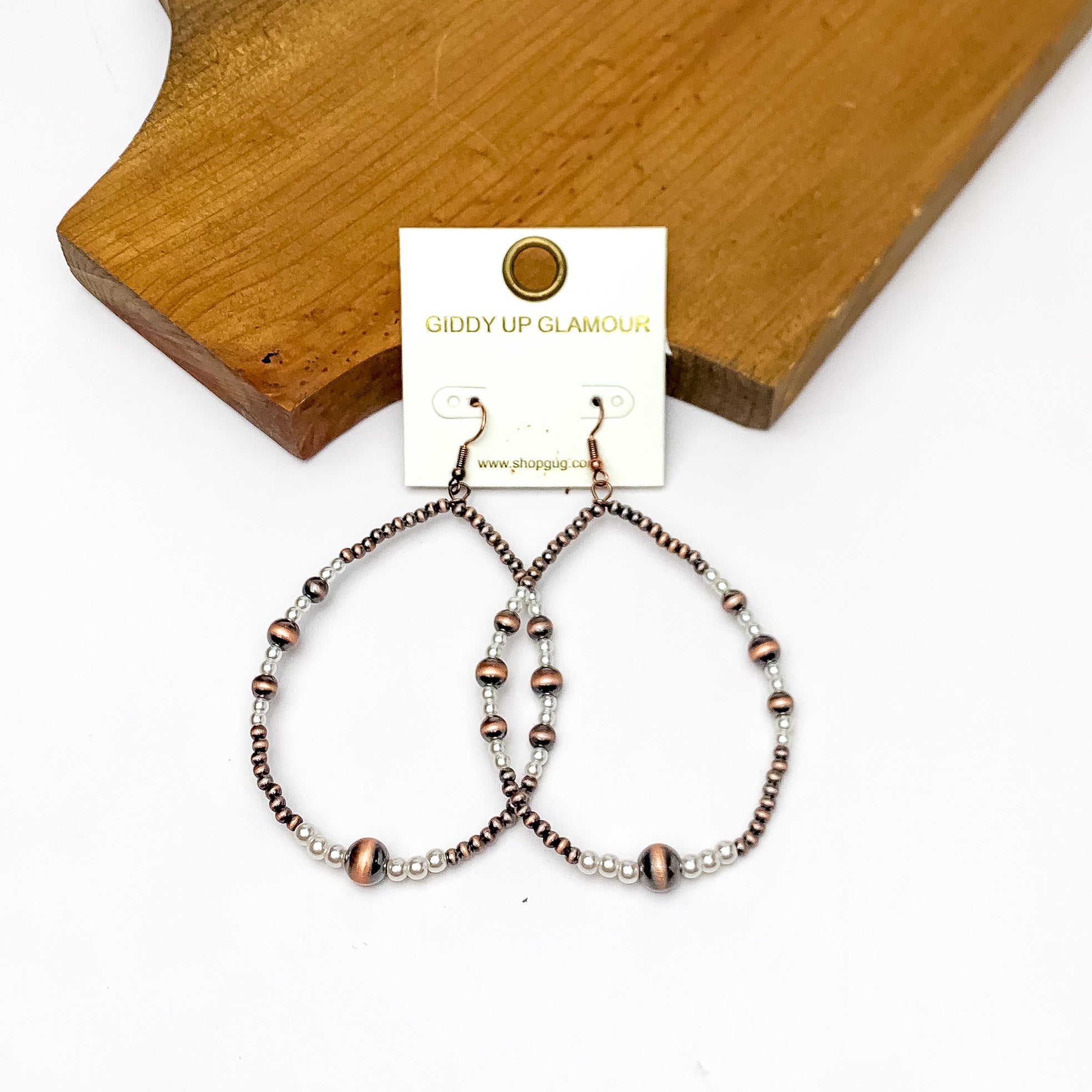Open Teardrop Earrings With Beads in Copper Tone and White. Pictured on a white background with the earrings against  wood piece.