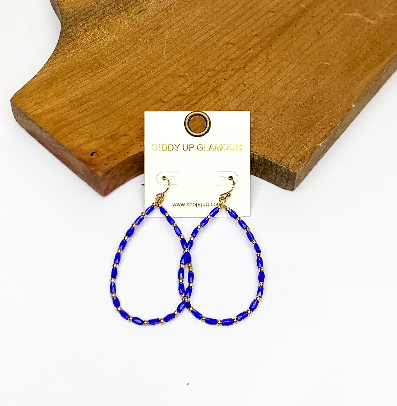 Royal Blue Beaded Open Drop Earrings with Gold Tone Spacers. Pictured on a white background with the earrings against a wood piece.