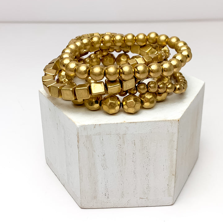 Set Of Five | Gold Tone Beaded Bracelets. Pictured on a white background with the bracelets on a podium.