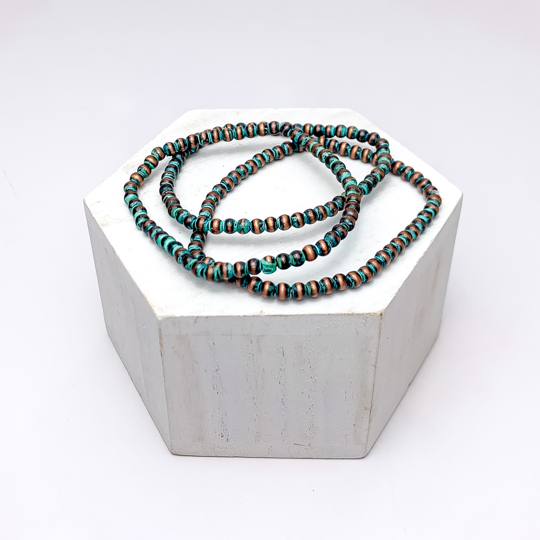 Set of Three | Stretchy Beaded Bracelets In Patina. Pictured on a white background with the bracelets on a podium.