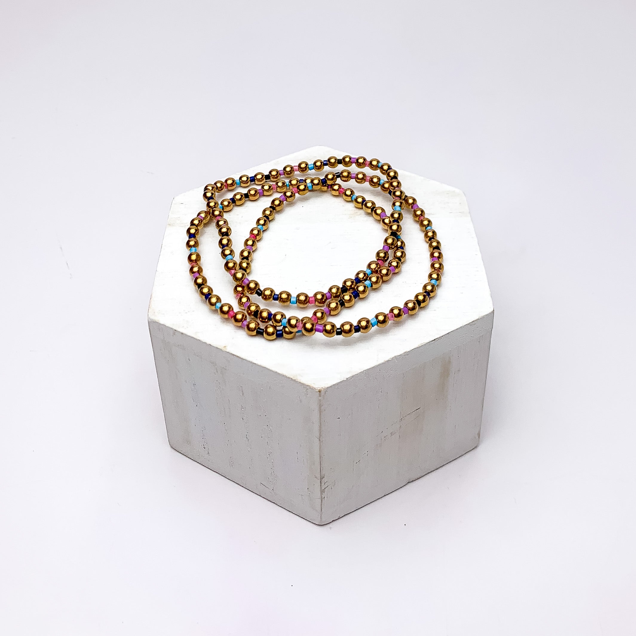 Set of Three | Stretchy Gold Tone Beaded Bracelets With Spacers in Multicolor. Pictured on a white background with the bracelets on a podium.