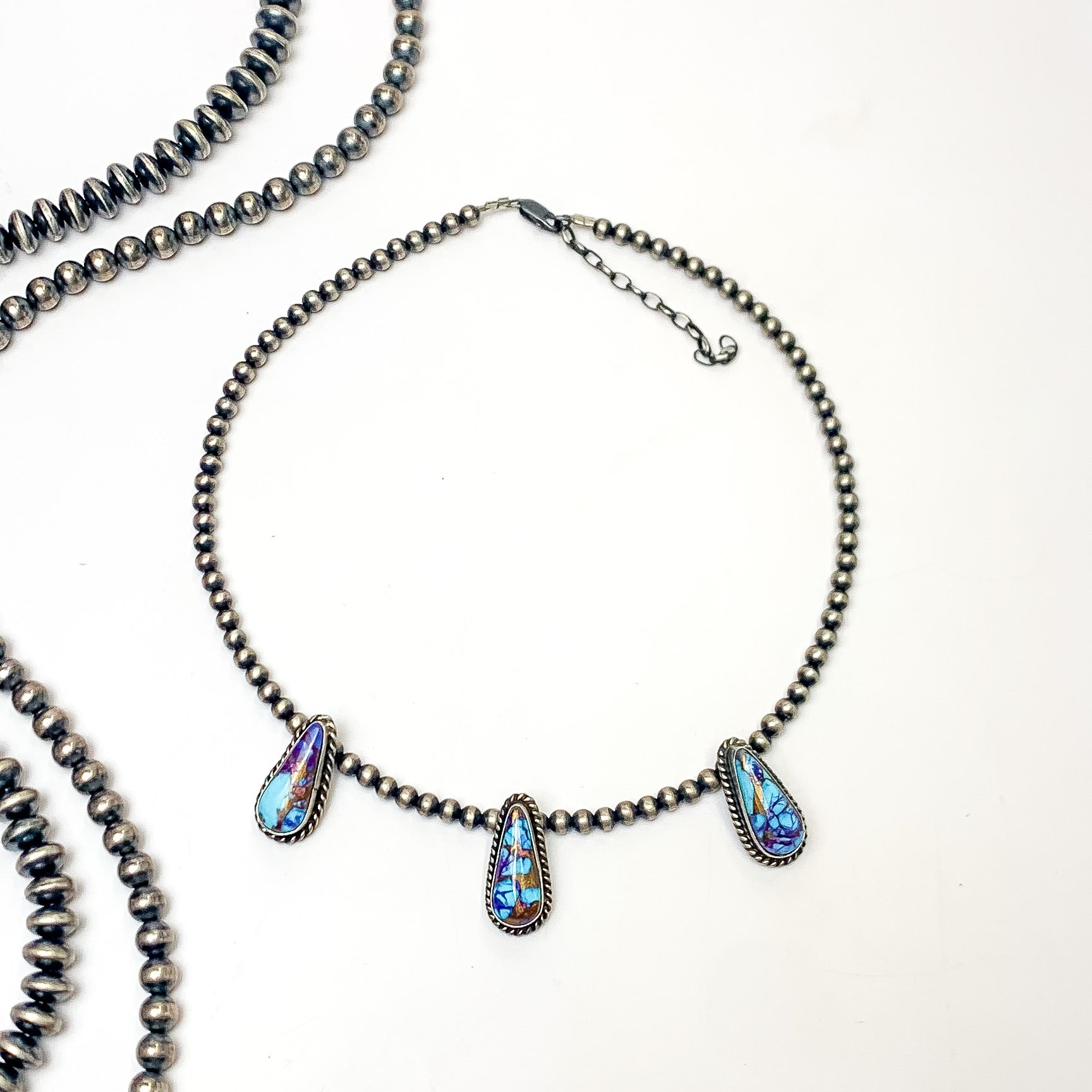 Pictured is a silver pearl beaded necklace with three teardrop stones. These stones are mojave turquoise remix stones. This necklace is pictured on a white background with silver beads on the left side. 