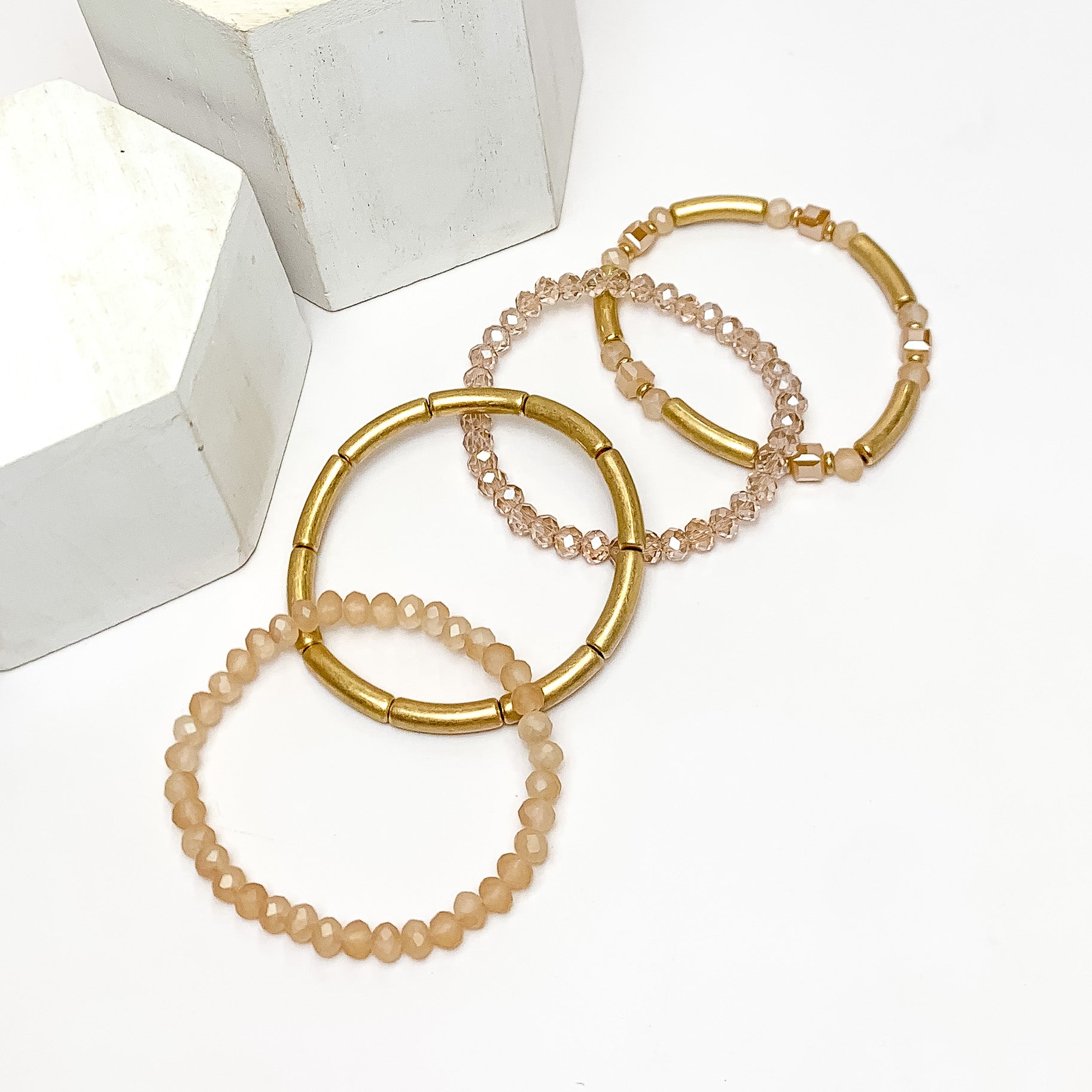 Set of Four | City Trip Beaded Bracelet Set in Gold Tone and Ivory. Pictured on a white background with two white podiums behind the bracelets.