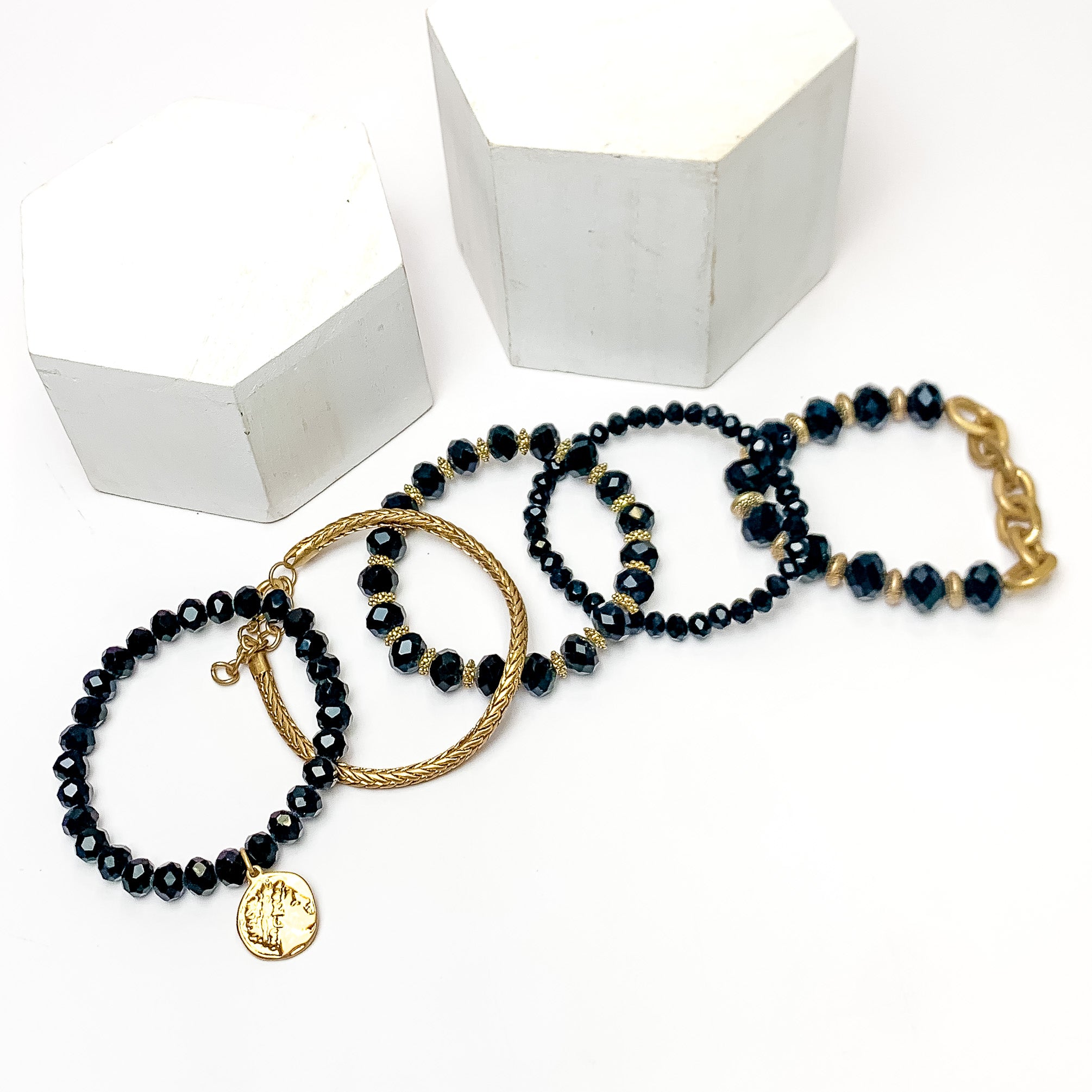 Set of Five | City Dreamer Gold Tone Bracelet Set in Black. Pictured on a white background with two white podiums behind the bracelets.