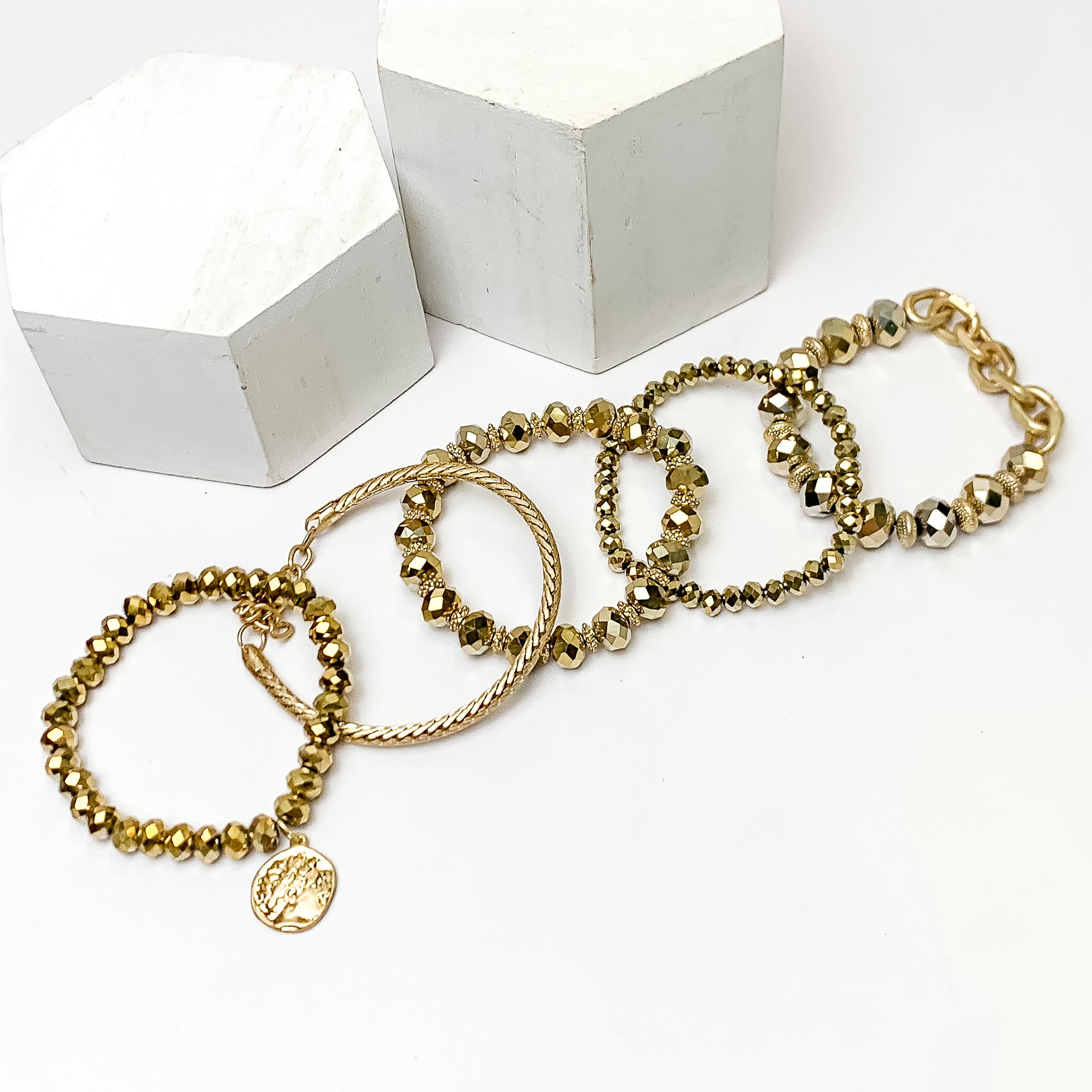 Set of Five | City Dreamer Gold Tone Bracelet Set. Pictured on a white background with two white podiums behind the bracelets.
