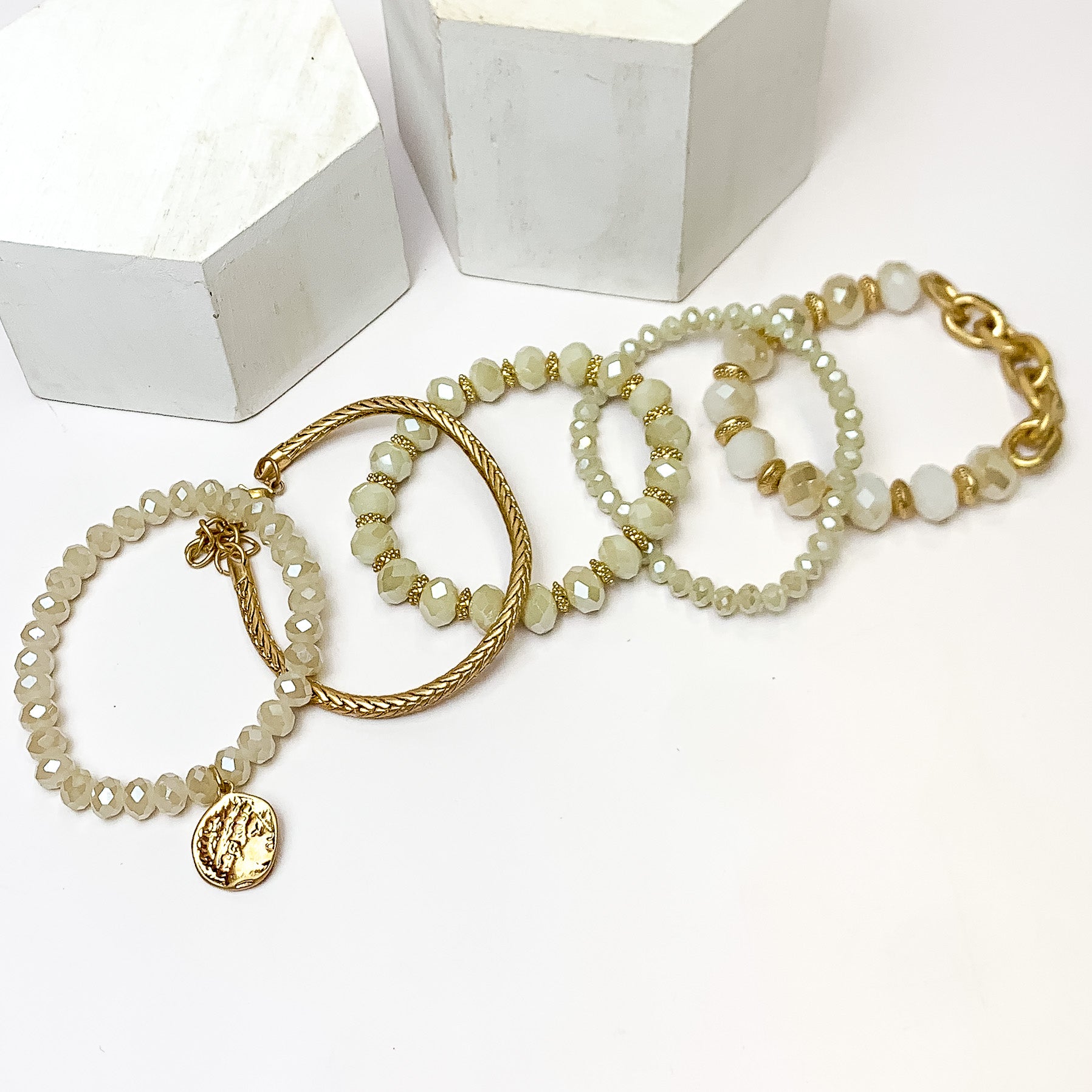 Set of Five | City Dreamer Gold Tone Bracelet Set. Pictured on a white background with two white podiums behind the bracelets.