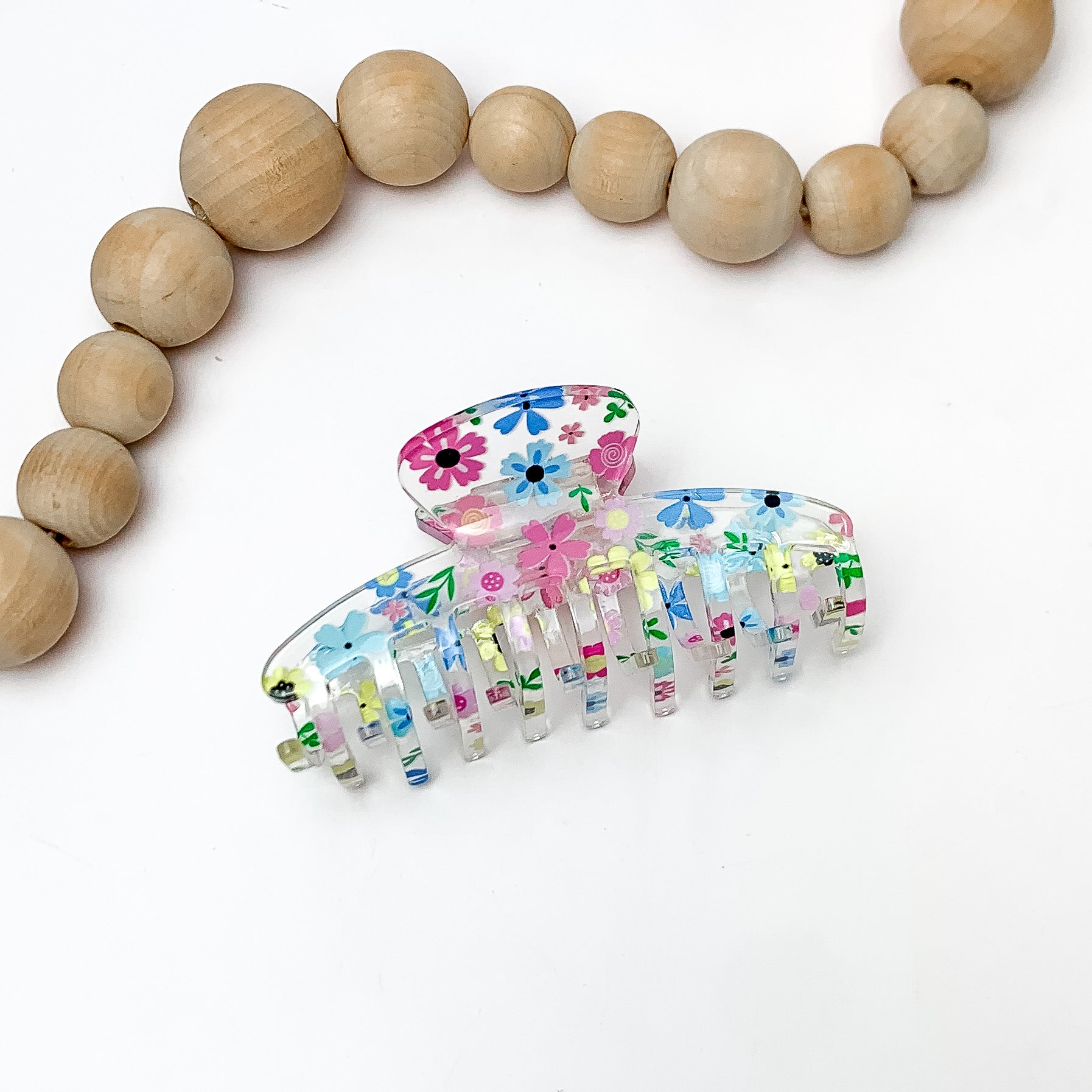 Flower Fields Hair Clip in clear with multicolor flowers. Pictured on a white background with wood beads above the hair clip.
