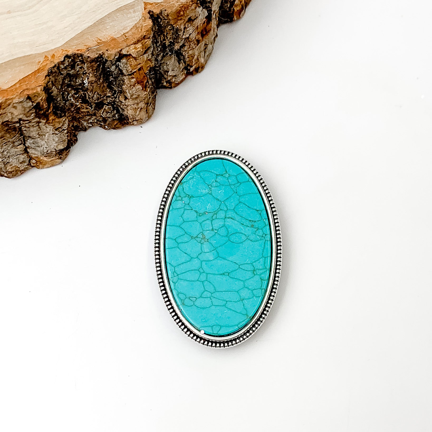 Turquoise Stone With Silver Tone Trim Oval Phone Grip. Pictured on a white background with a wood piece in the top left corner.