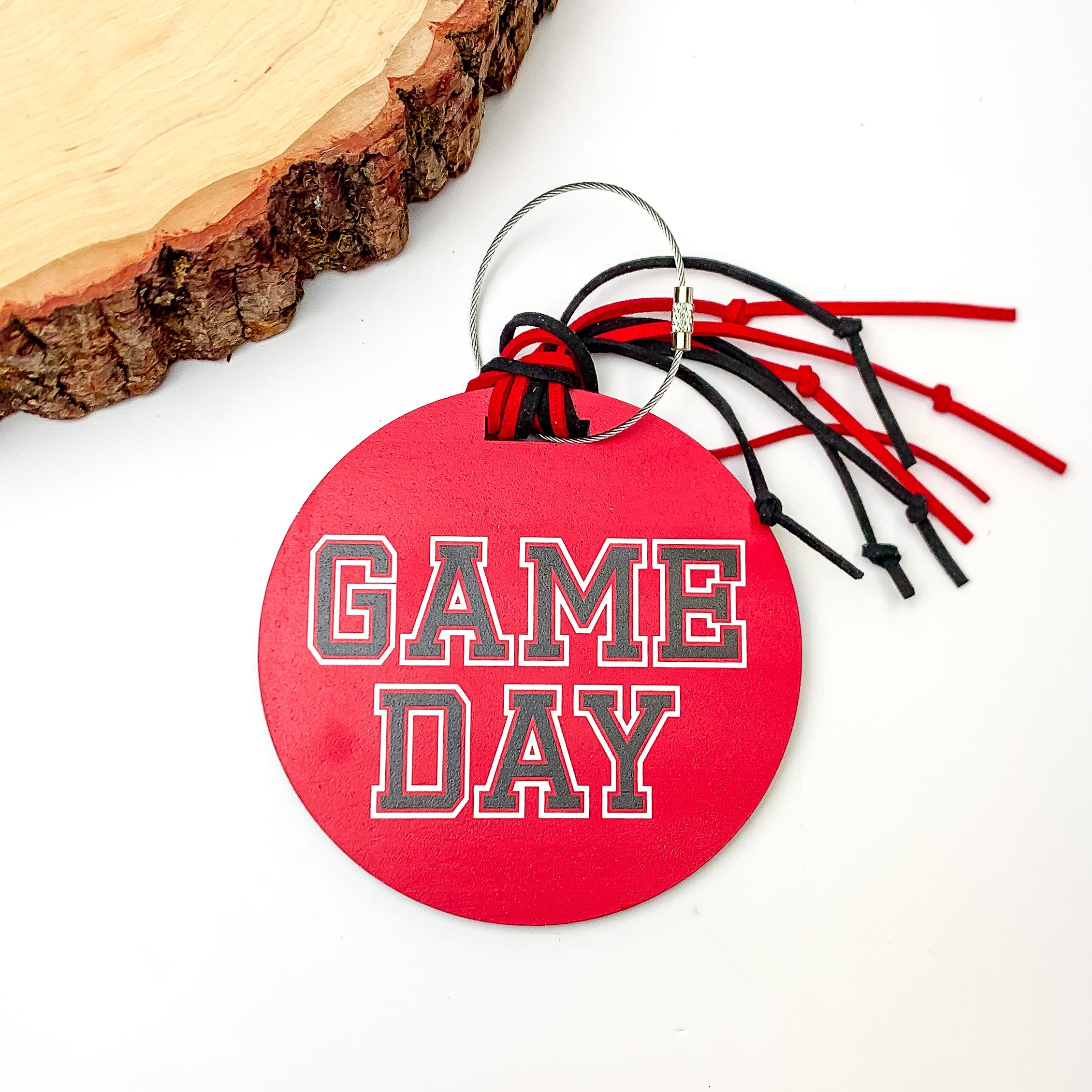 Game Day Luggage Tag in Red With Black Details. Pictured on a white background with a wood piece in the top left corner.