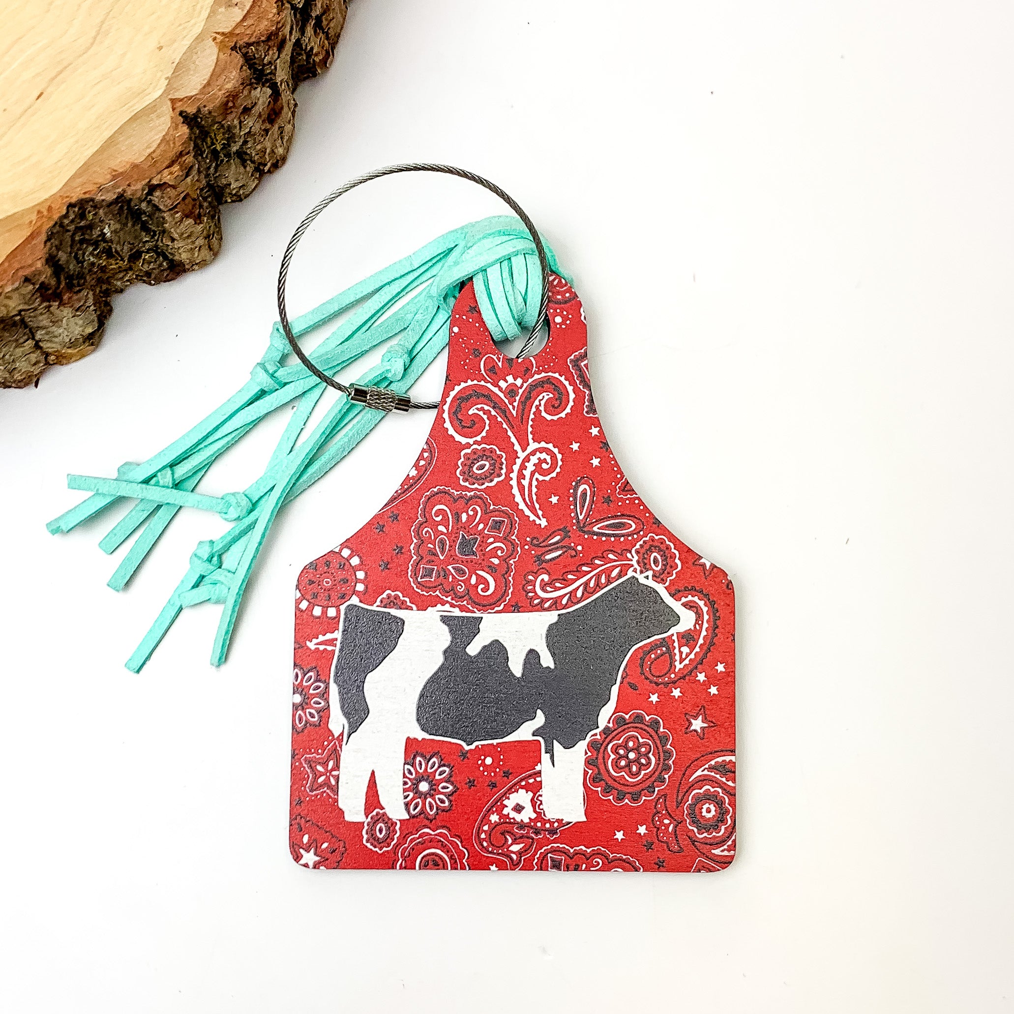 Red and Turquoise Luggage Tag With Cow. Pictured on a white background with a wood piece in the top left corner.