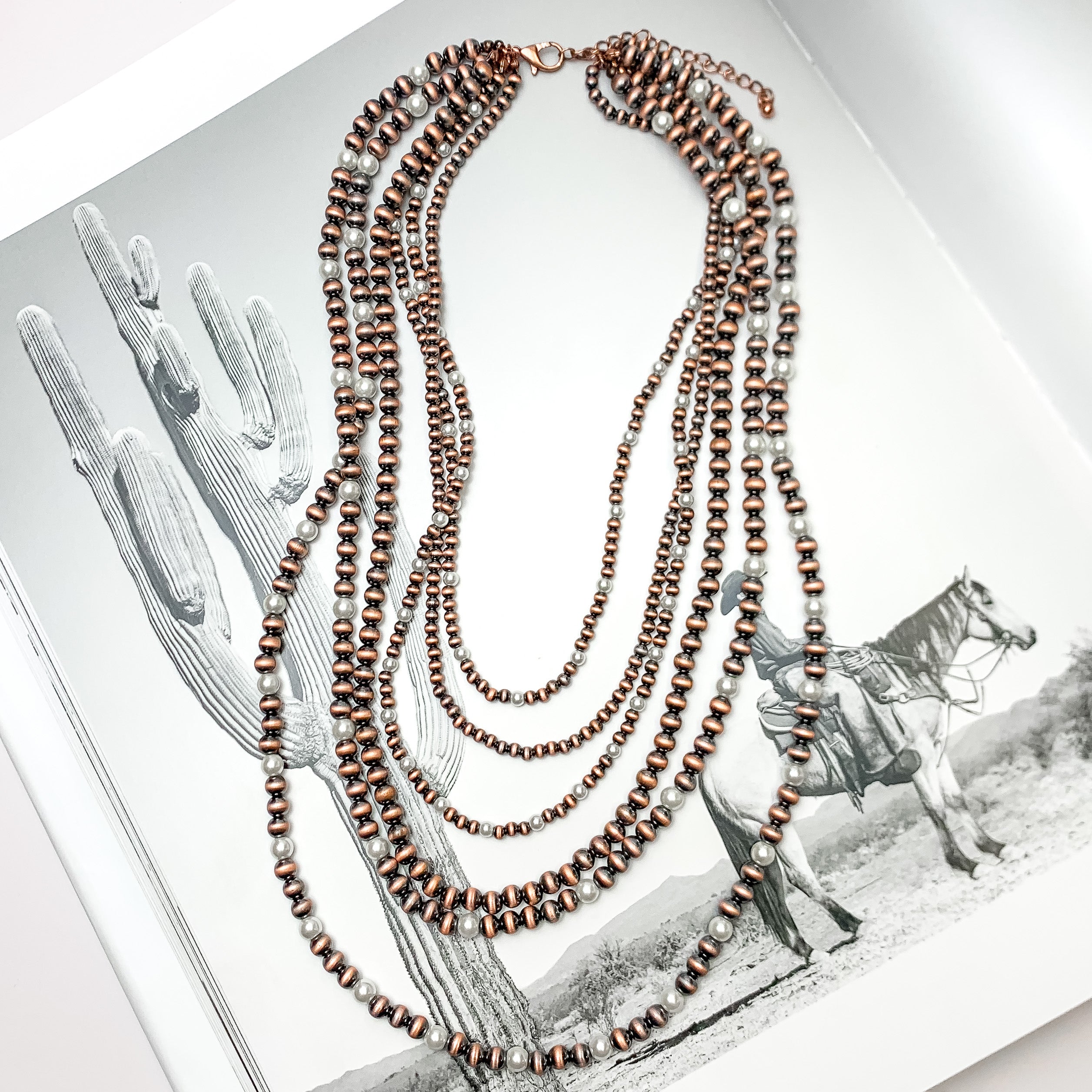 Six Strand Faux Navajo Pearl Necklace in Copper Tone with White Pearl Beads. Pictured on a western background.