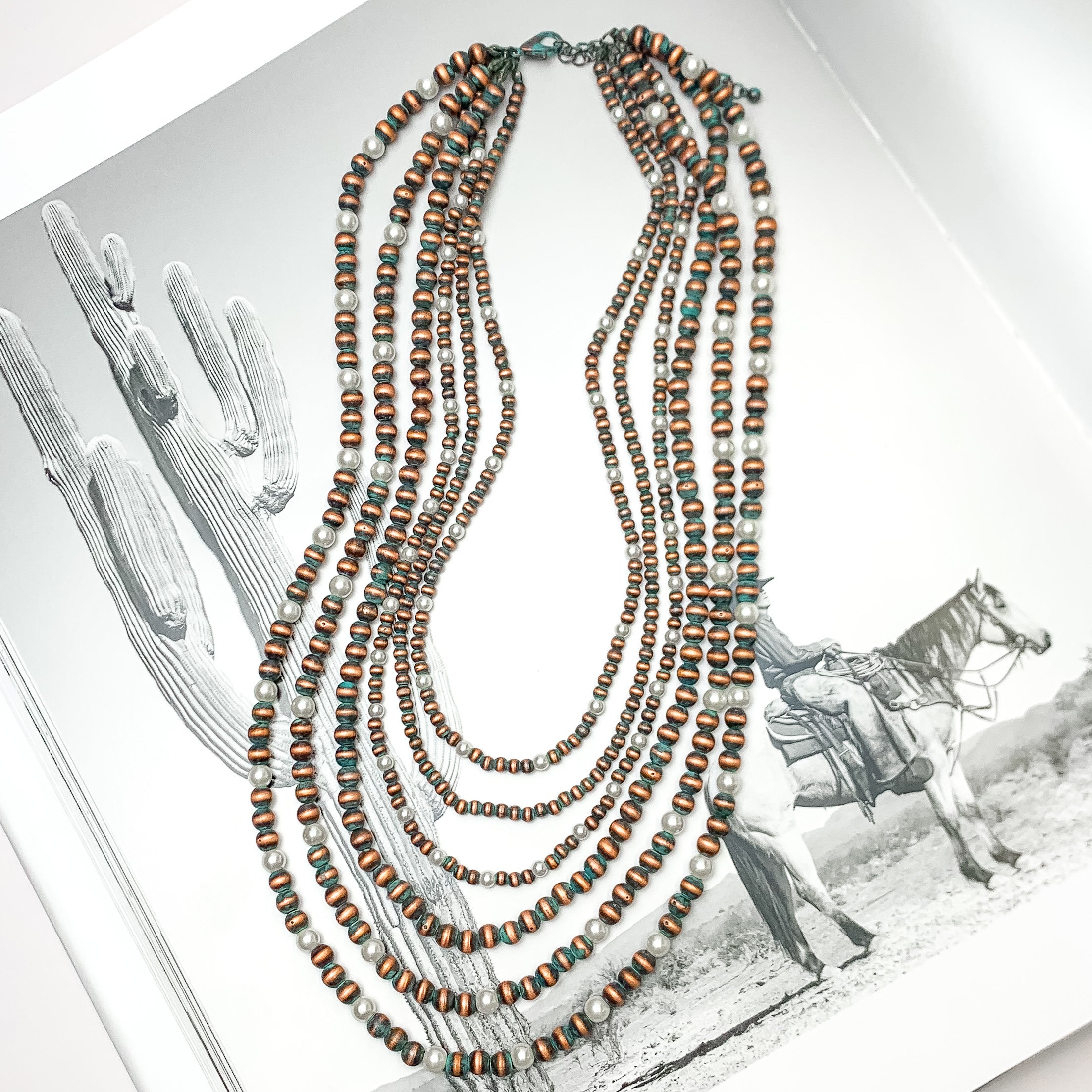 Six Strand Faux Navajo Pearl Necklace in Patina Tone with White Pearl Beads. Pictured on a western background.
