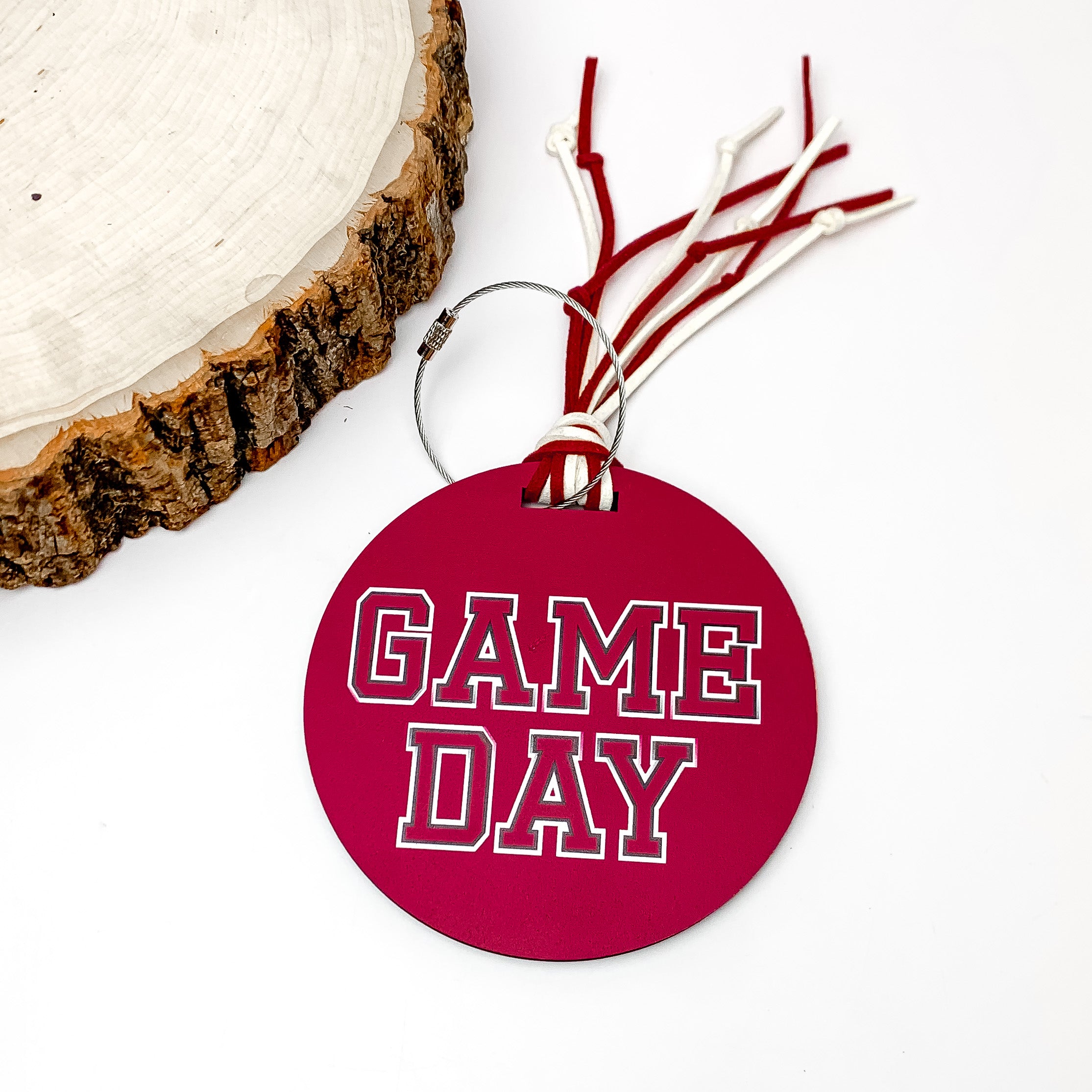 Game Day Luggage Tag in Maroon With White Details. Pictured on a white background with a wood piece in the top left corner.