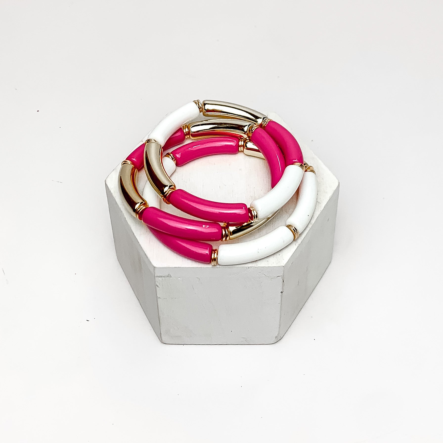 Set of Three | Thin Tube Bracelets in Hot Pink, White, And Gold Tone. Pictured on a white background with the bracelets on a podium.