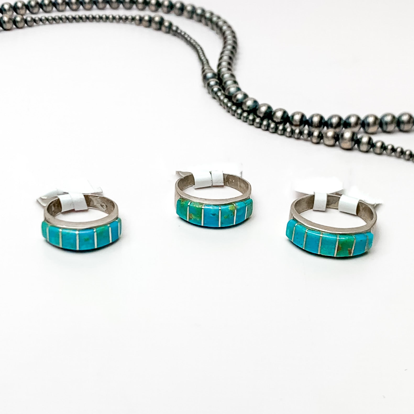 Three silver rings with green turquoise stones pictured on a white background with silver beads. 