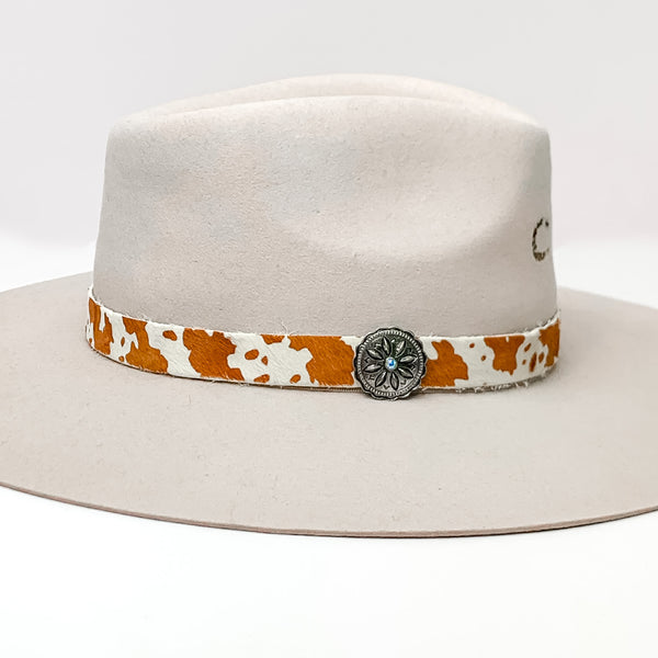 Cow Print Hat Band with Silver Tone Charm in Brown, and Ivory. Pictured on a white background with the band around a light tan/ brown hat.