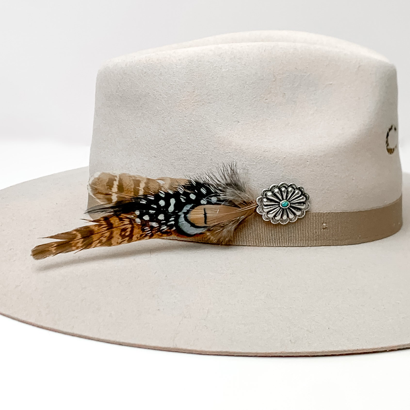 Oval Concho With Mixed Brown and Black Feathers Hat Pin With Turquoise Stone. Pictured on a white background with the pin on the side of a light grey/ brown hat.