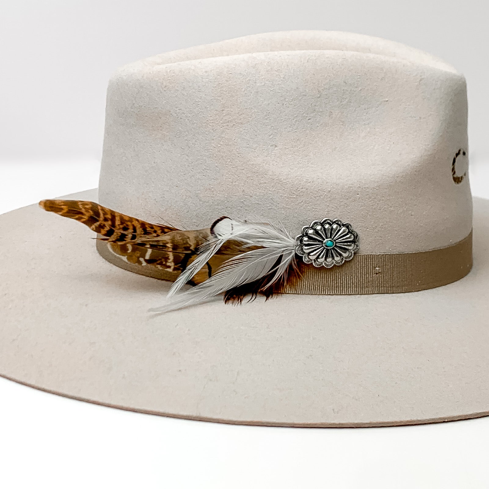 Oval Concho With Mixed Brown and White Feathers Hat Pin With Turquoise Stone. Pictured on a white background with the pin on the side of a light grey/ brown hat.