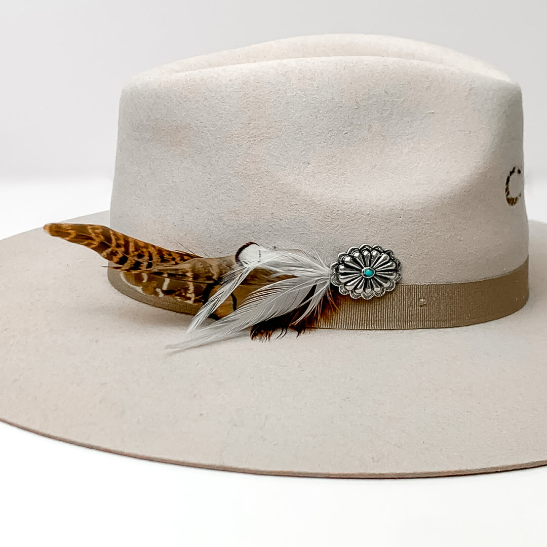 Oval Concho With Mixed Brown and White Feathers Hat Pin With Turquoise Stone. Pictured on a white background with the pin on the side of a light grey/ brown hat.