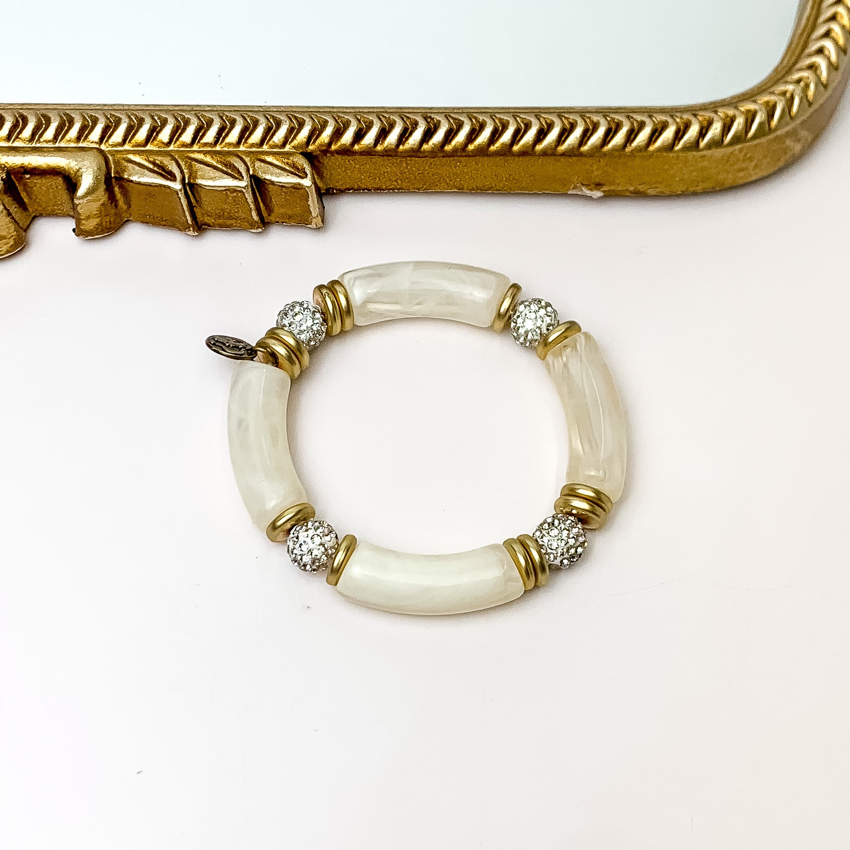 Pictured is one bracelet that has ivory bamboo beads, gold beads, and clear crystal beads. This bracelet is pictured in front of a gold mirror on a white background. 