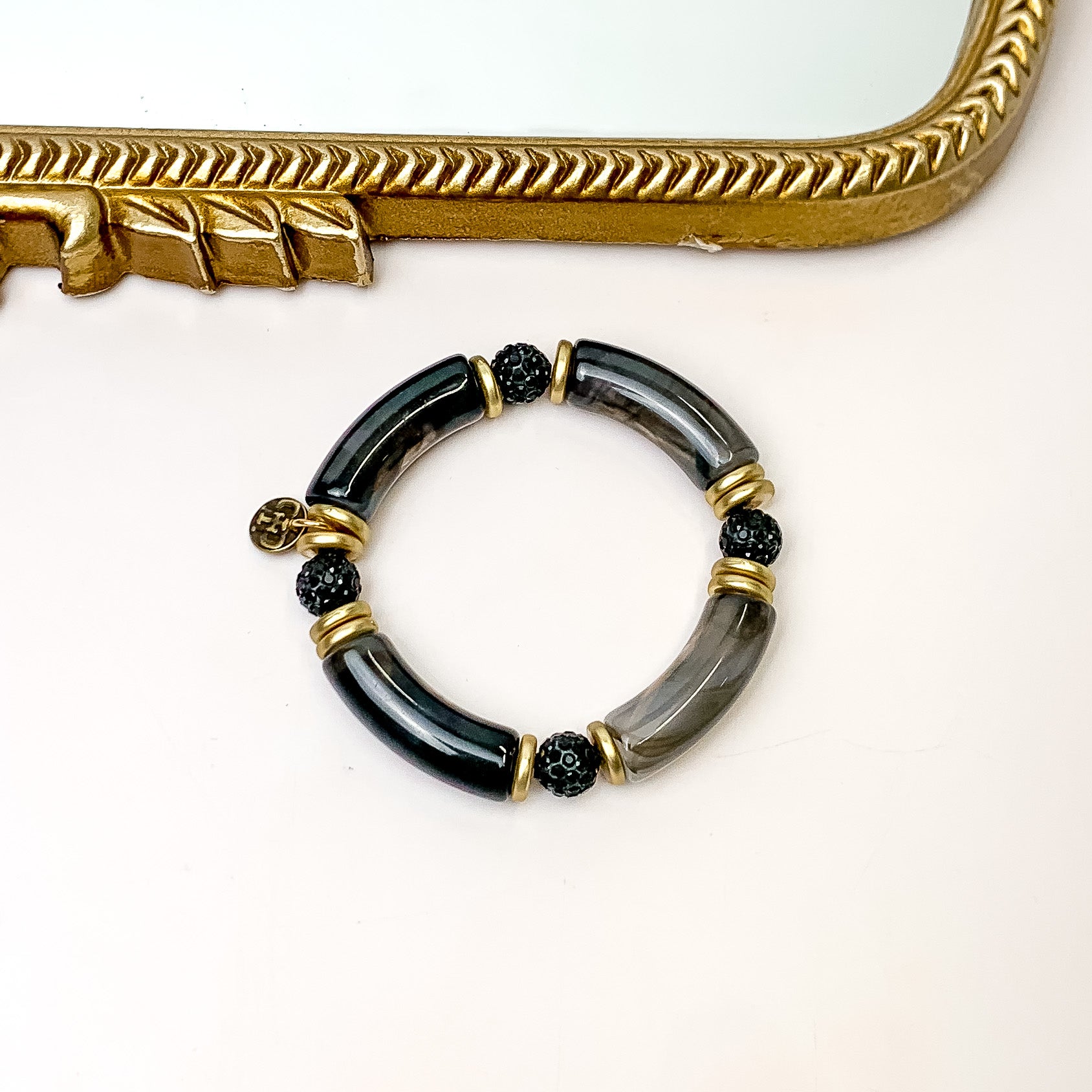 Pictured is one bracelet that has black bamboo beads, gold beads, and black crystal beads. This bracelet is pictured in front of a gold mirror on a white background. 