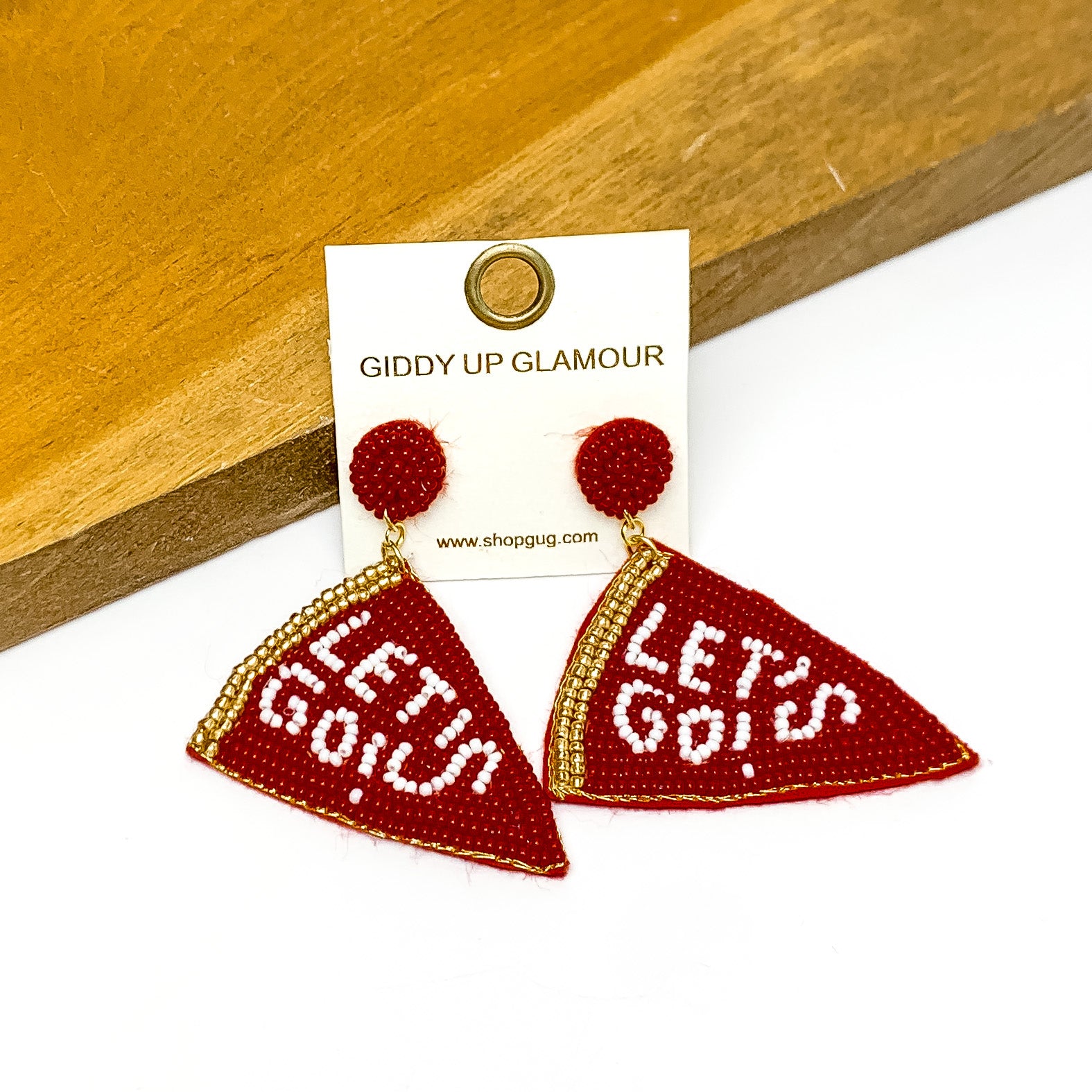 Lets Go Beaded Flag Earrings in maroon. Pictured on a white background with the earrings laying against a wood piece.
