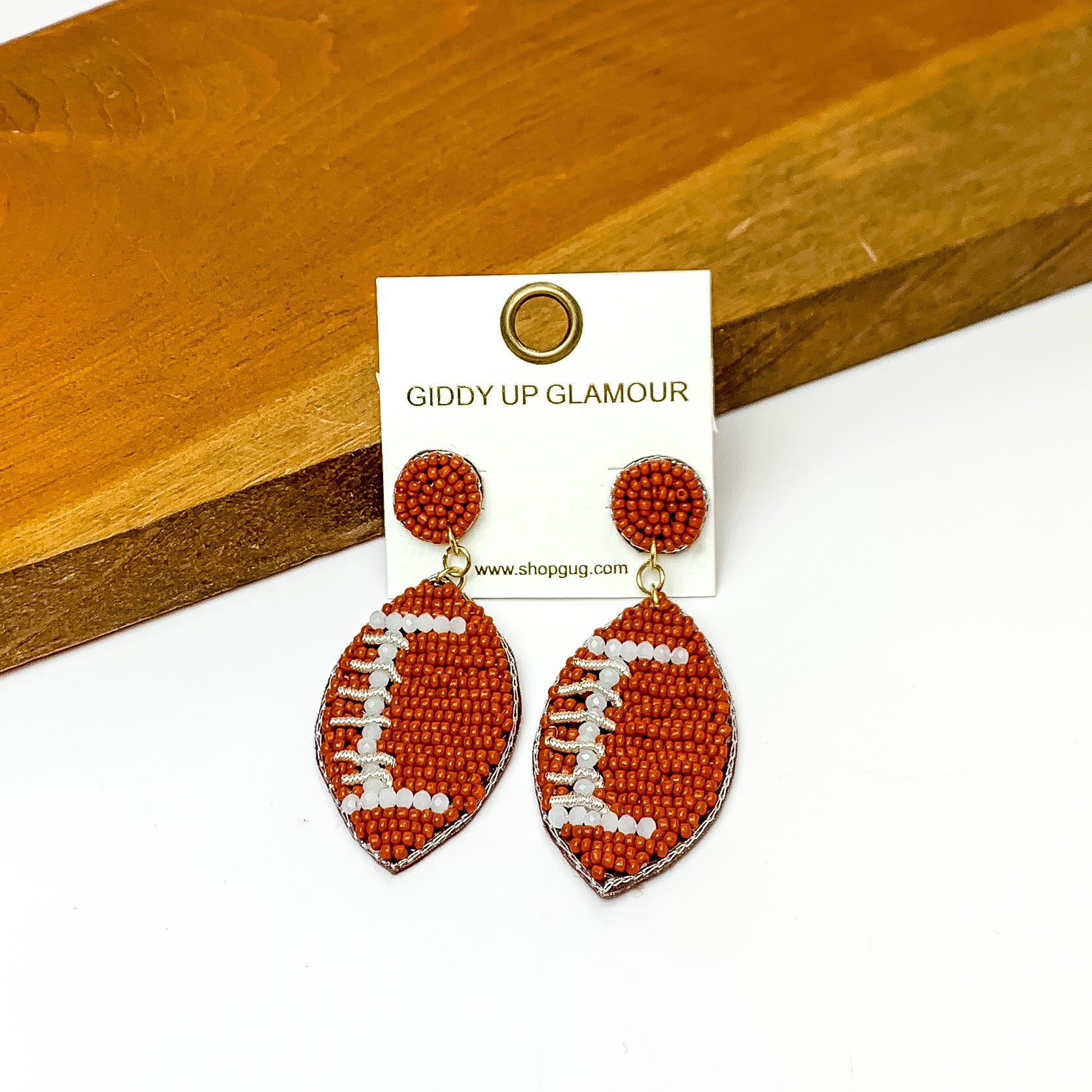 Football Post Beaded Earrings in Brown. Pictured on a white background with the earrings laying against a wood piece.