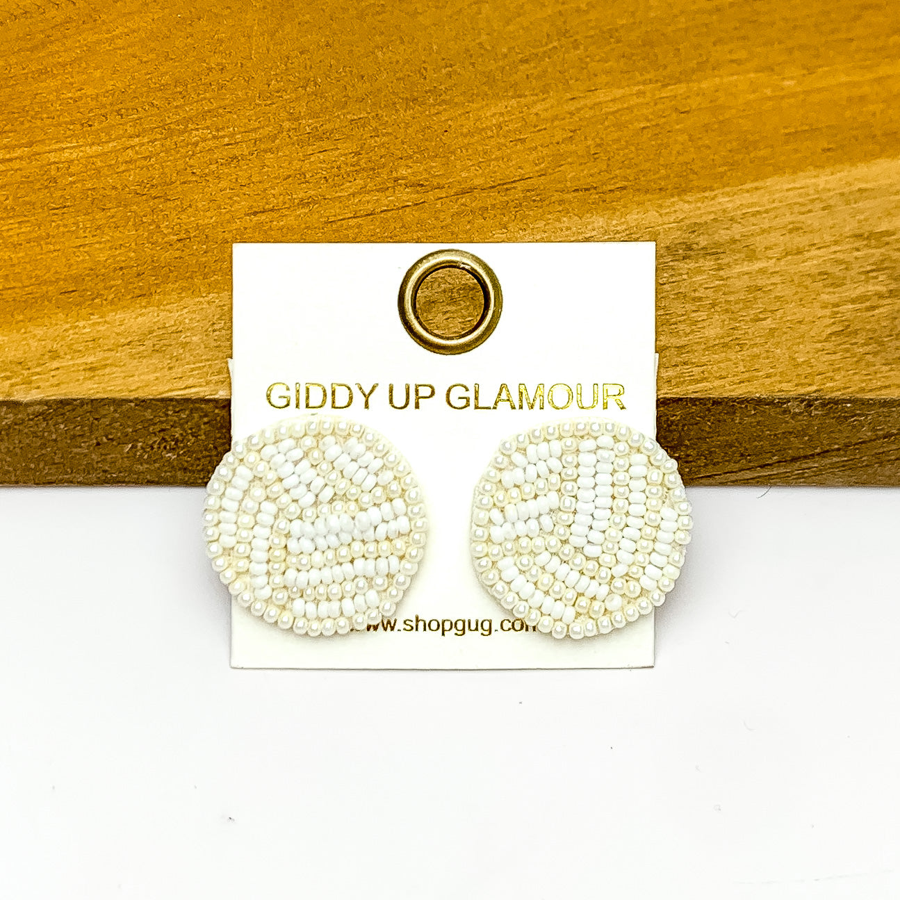 Let's Get Sporty Seed Bead Volleyball Stud Earrings. Pictured on a white background with the earrings laying on a wood piece.