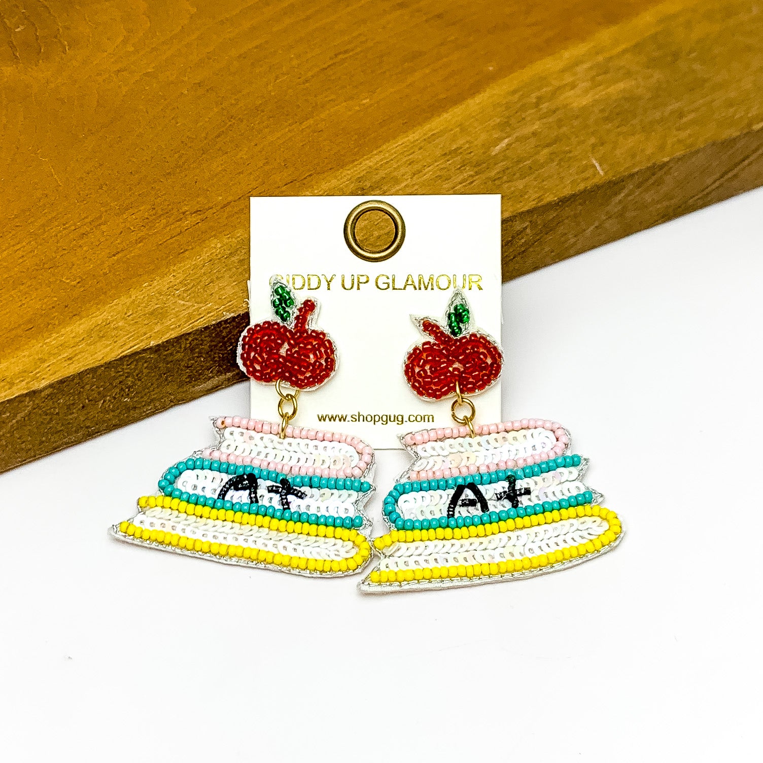 Stacked Books With Apple Post in Multicolor. Pictured on a white background with the earrings against a wood piece.