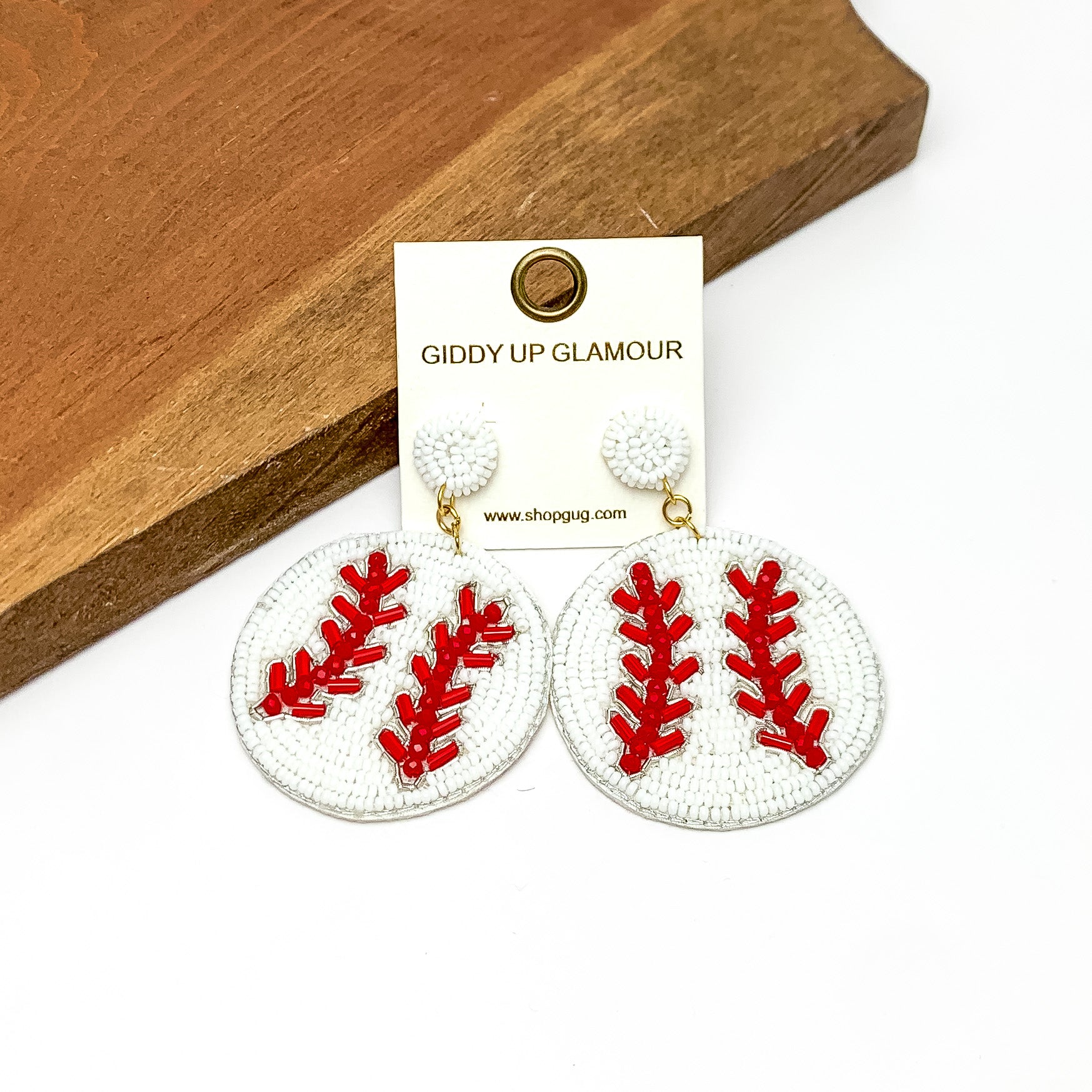 Baseball Circular Beaded Earrings in White and Red. Pictured on a white background with the earrings against a wood piece.