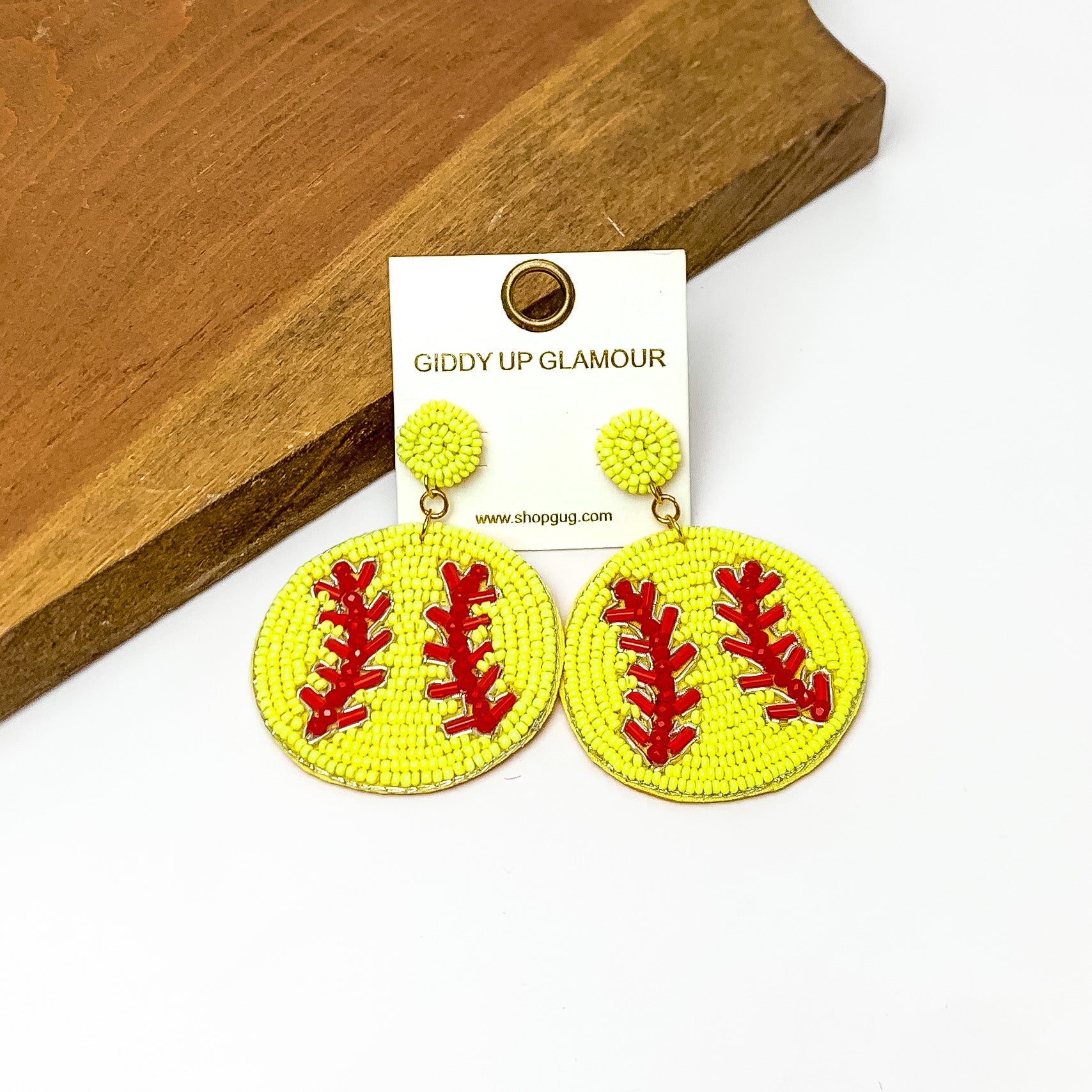 Softball Circular Earrings in Yellow. Pictured on a white background with the earrings against a wood piece.