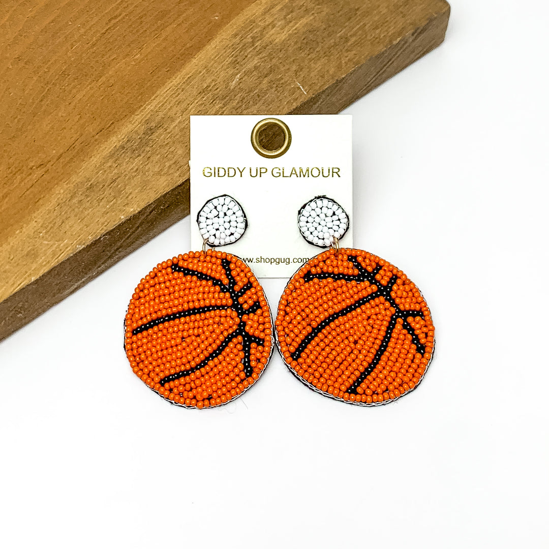 Basketball Circular Beaded Earrings in Brown. Pictured on a white background with the earrings against a wood piece.