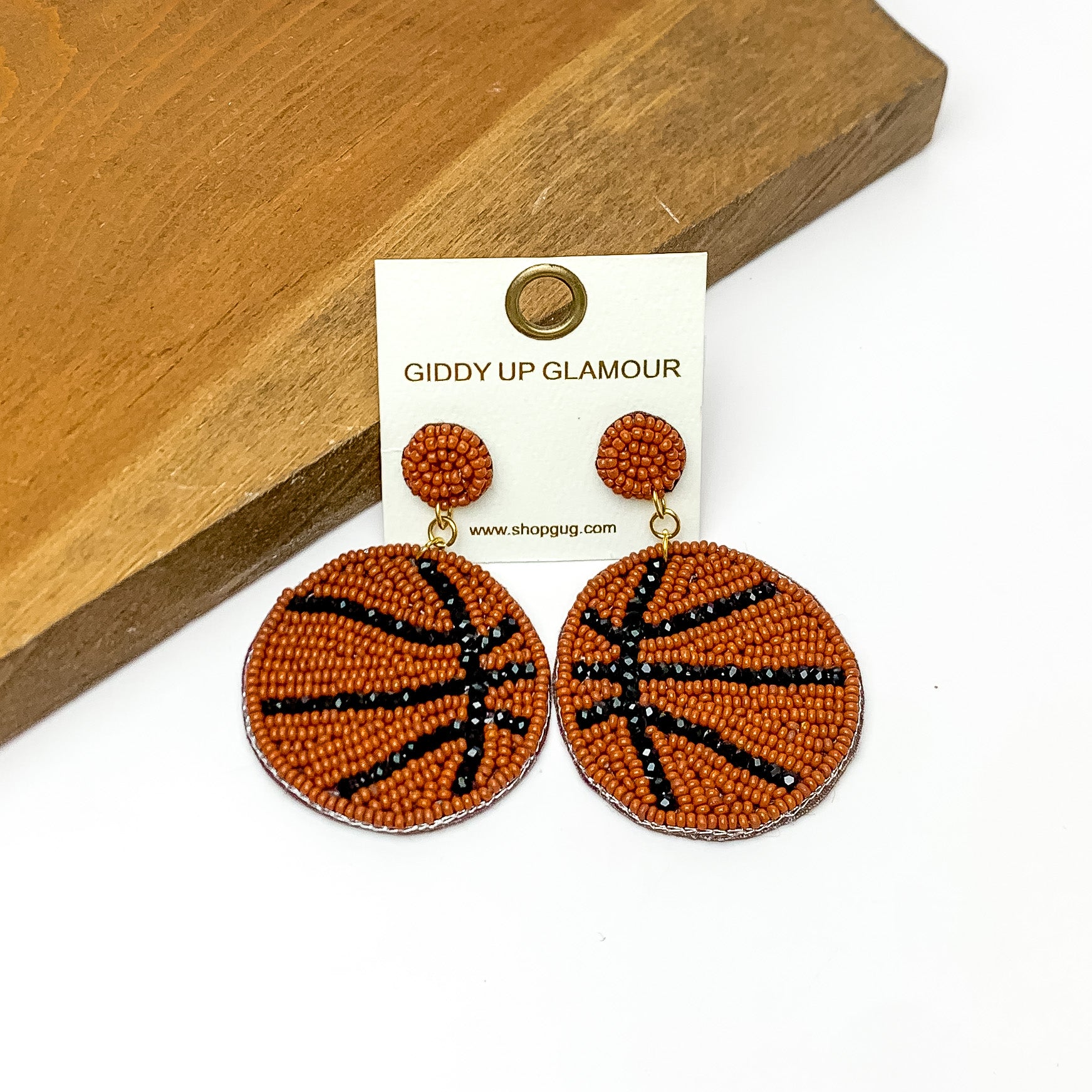 Basketball Circular Beaded Earrings in Brown. Pictured on a white background with the earrings against a wood piece.