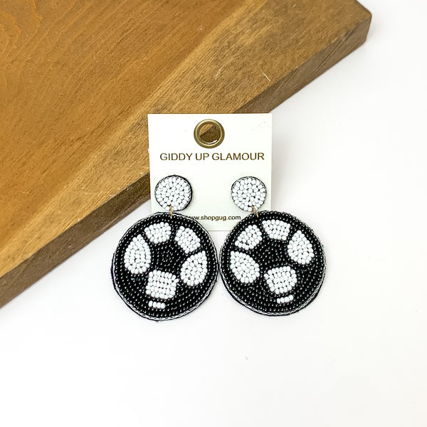 Soccer Ball Circular Beaded Earrings in Black. Pictured on a white background with the earrings against a wood piece.