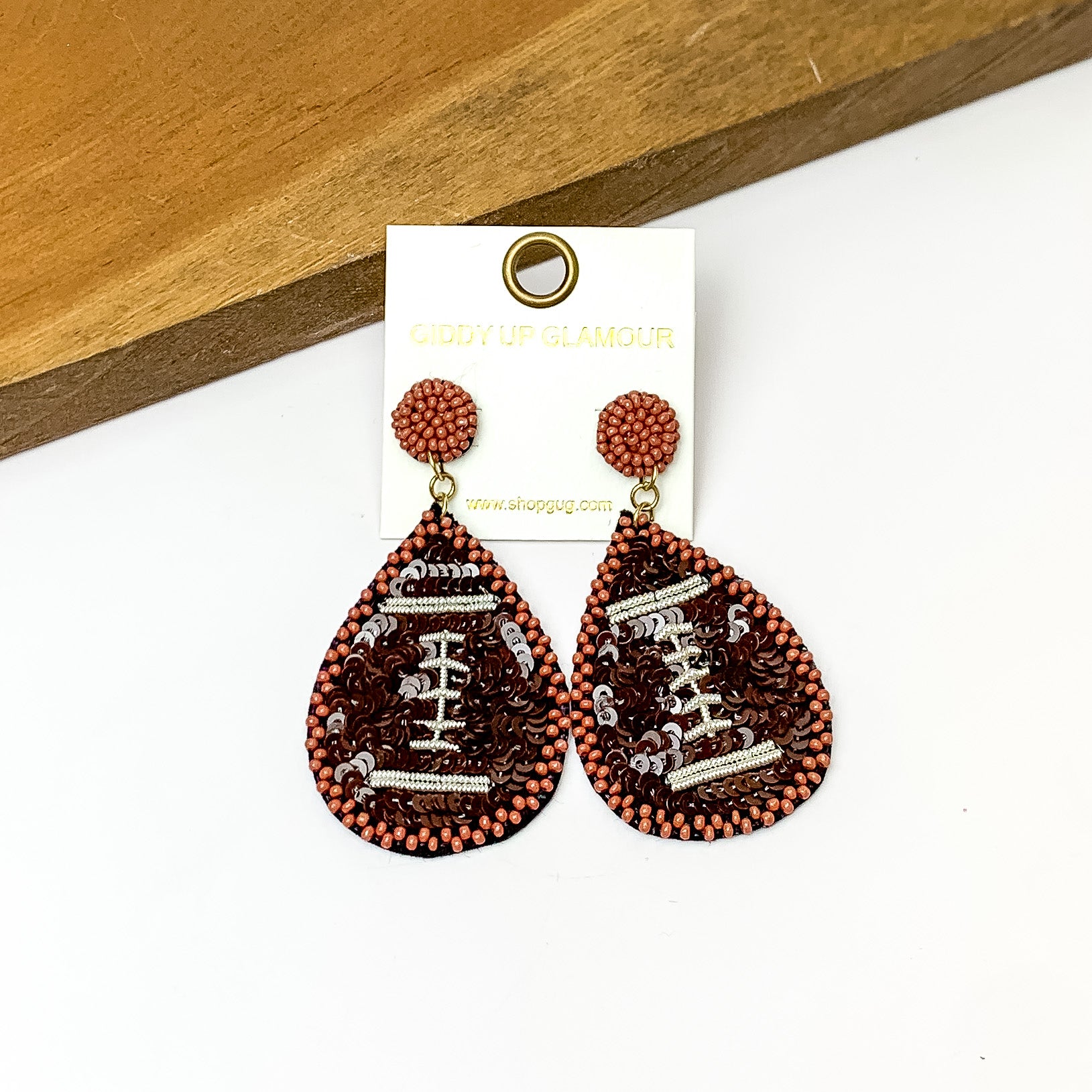 Football Teardrop Earrings With Sequins in Brown. Pictured on a white background with the earrings against a wood piece.