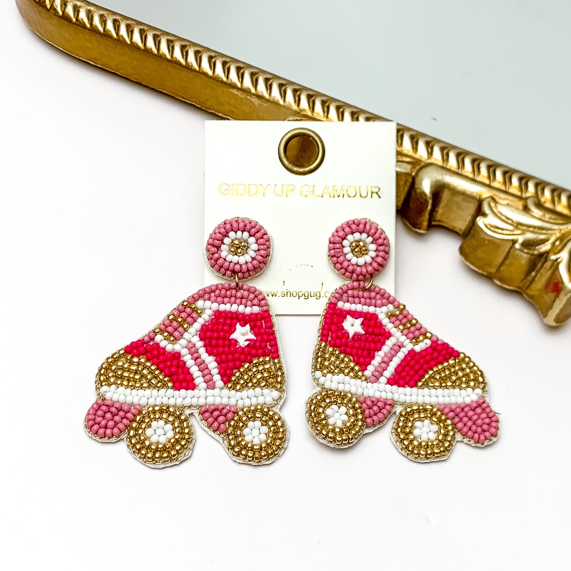 Roller Girl Beaded Roller Skate Earrings in Pink. Pictured on a white background with the earrings laying against a mirror with a gold trim.