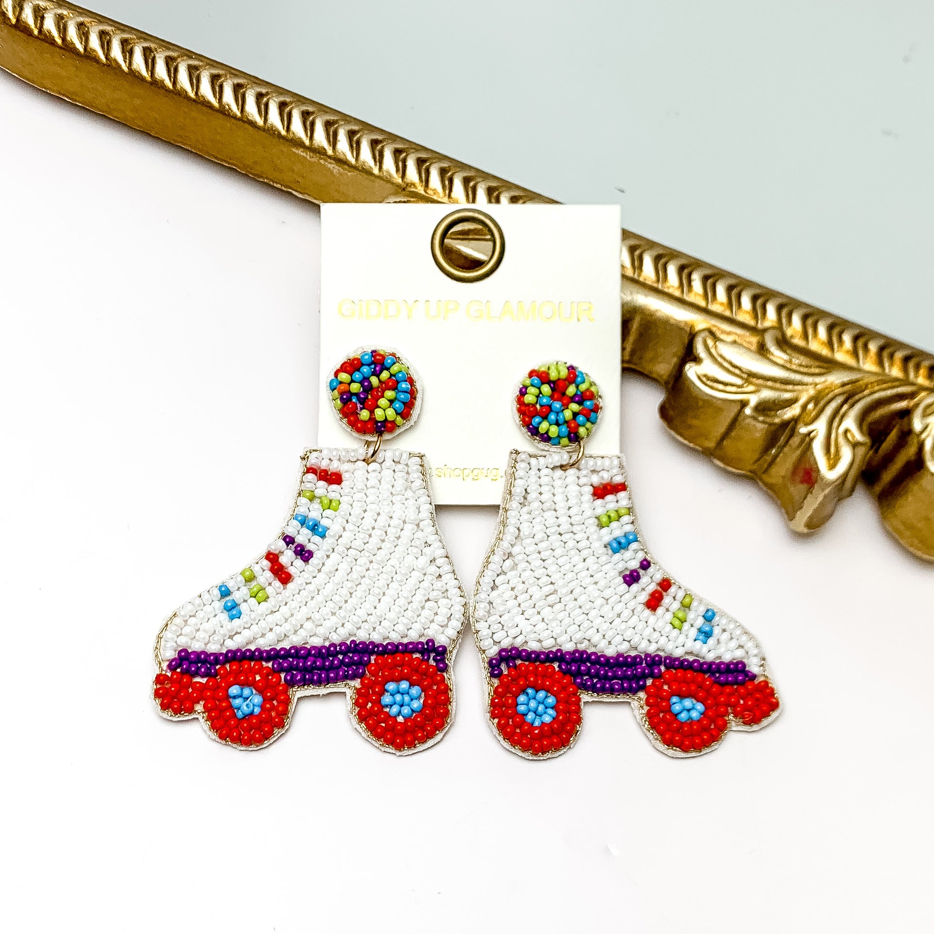 Roller Girl Beaded Roller Skate Earrings in Multicolor. Pictured on a white background with the earrings laying against a mirror with a gold trim.